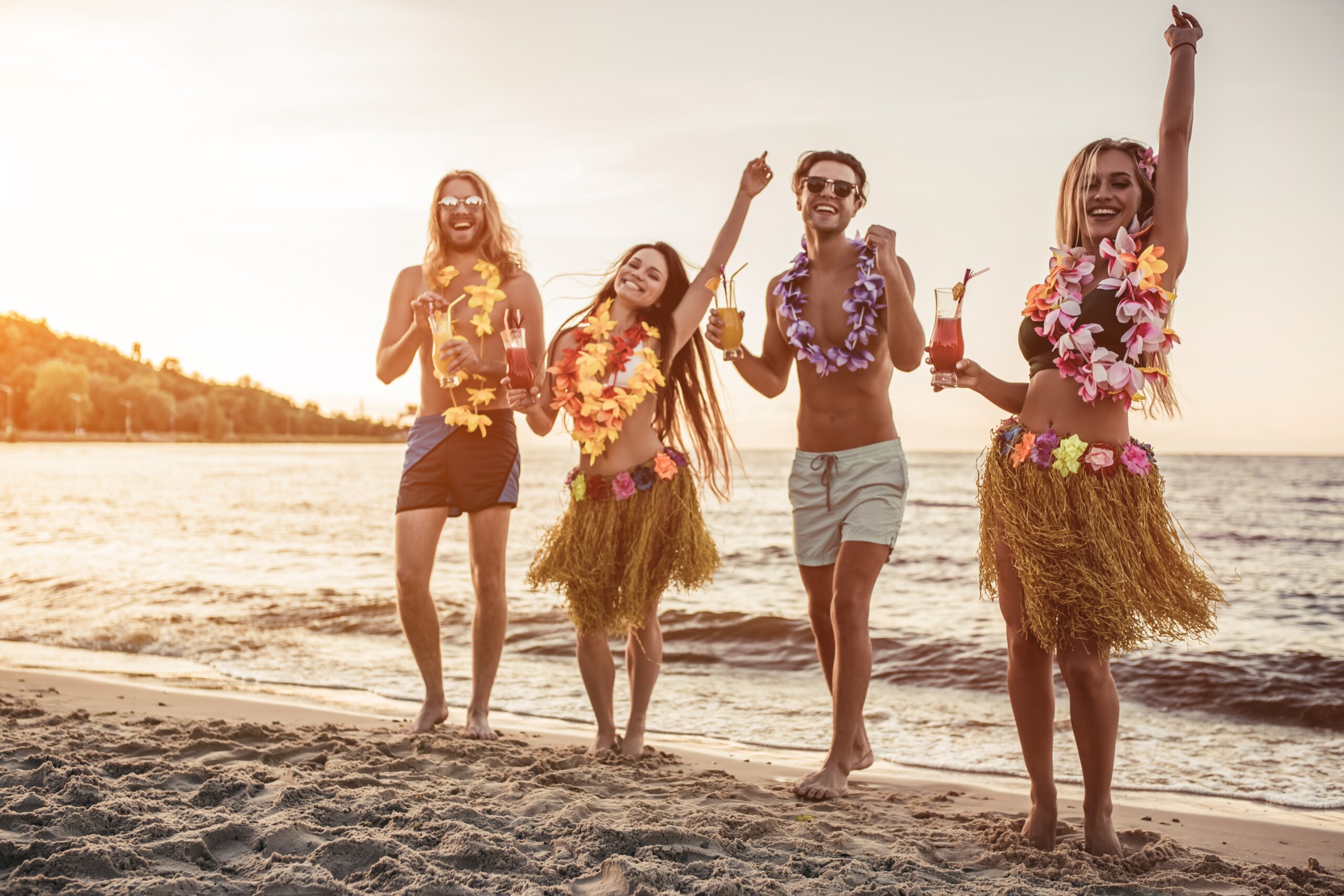 Friends wearing leis celebrating on the beach at sunset with drinks