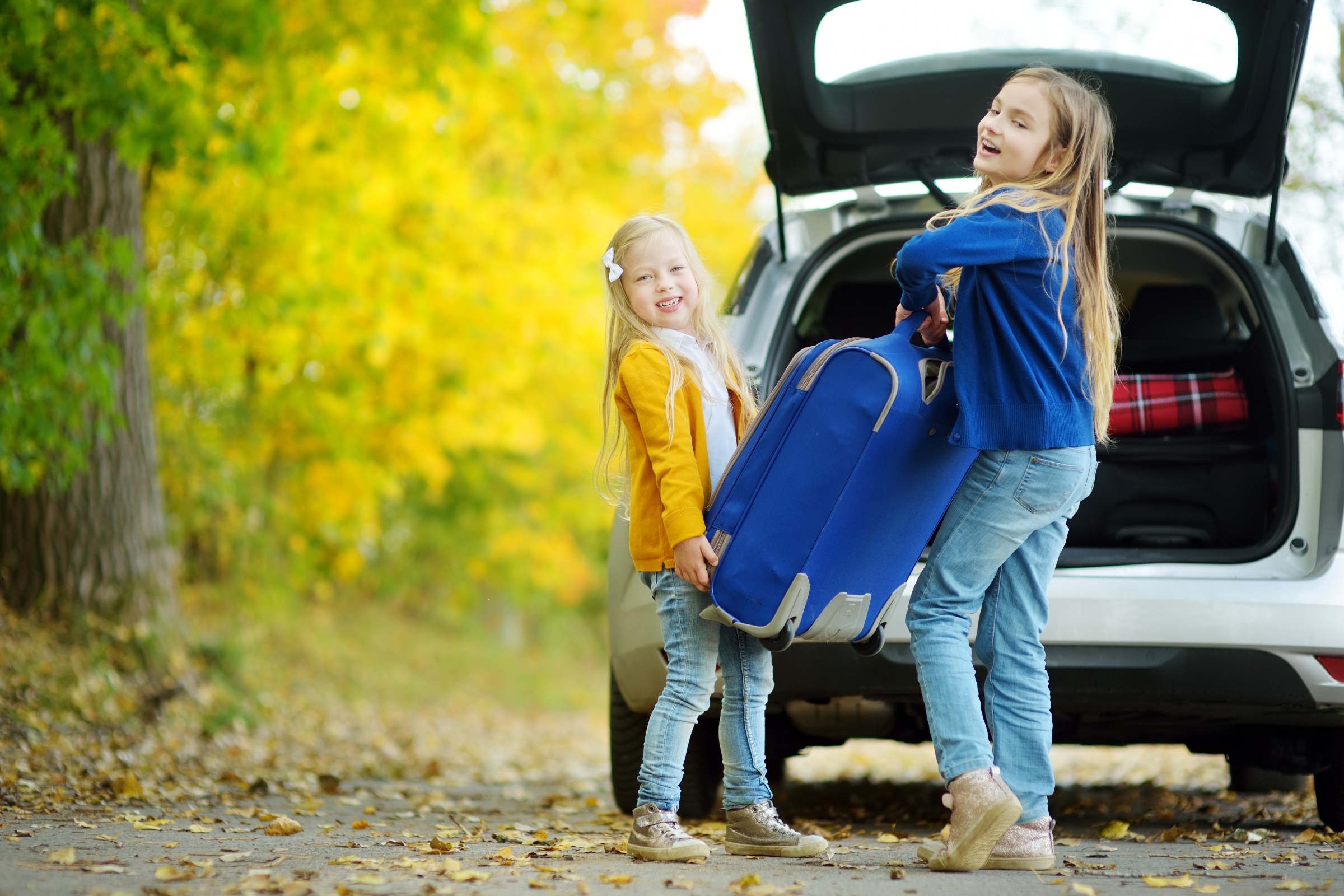 Two adorable girls with a suitcase going on vacations with their parents. Two kids looking forward for a road trip or travel. Autumn break at school.
