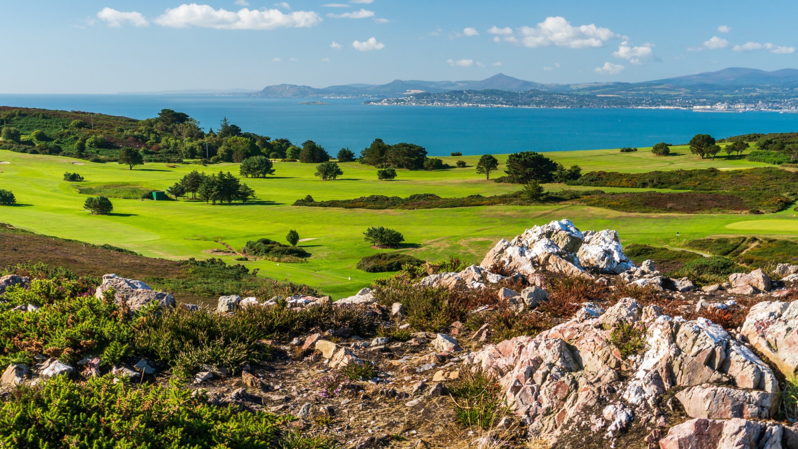 Colourful landscape with rocks, green grass and blue sea on a beautiful summer day. View over a golf course as seen from the top of Ben of Howth, Dublin, Ireland. 