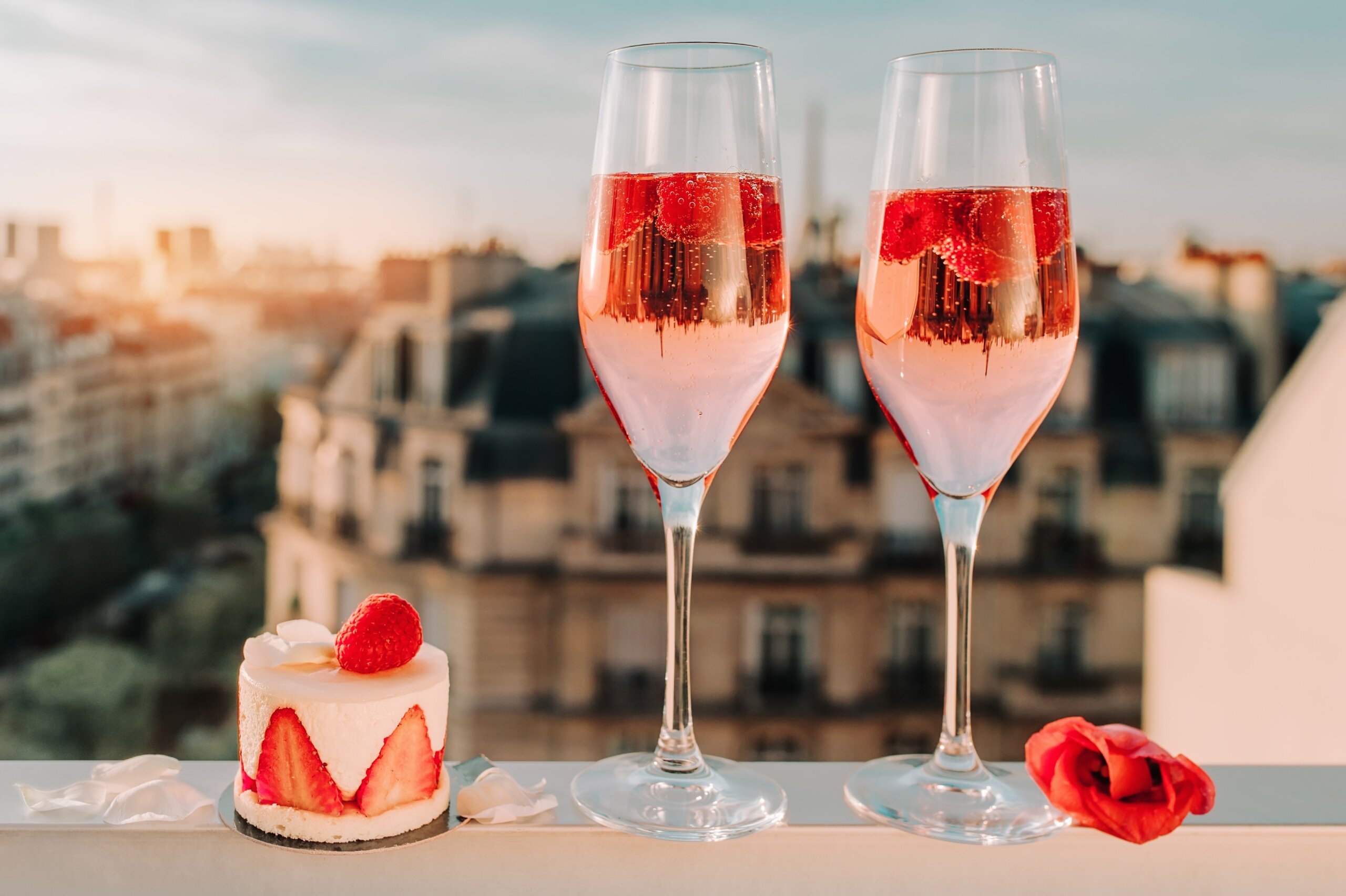 Paris luxury lifestyle. Pink champagne in two glasses, traditional french cake with strawberries on a balcony on the sunset