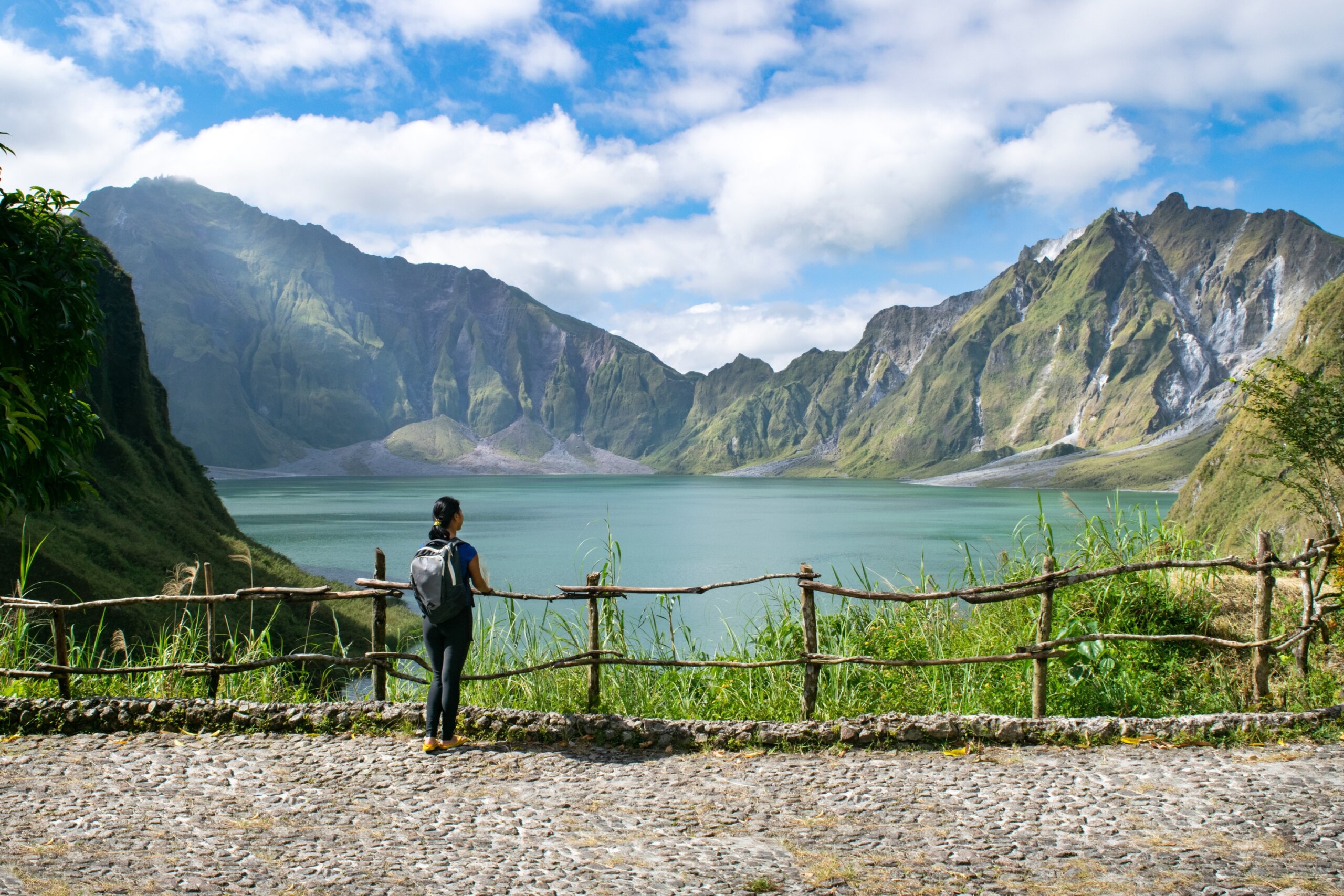 Young Asian girl stands at overlook near crater of Mount Pinatubo, featuring a large lake in between towering volcanic peaks - Mount Pinatubo, Philippines - one of the world’s most earthquake-prone regions.