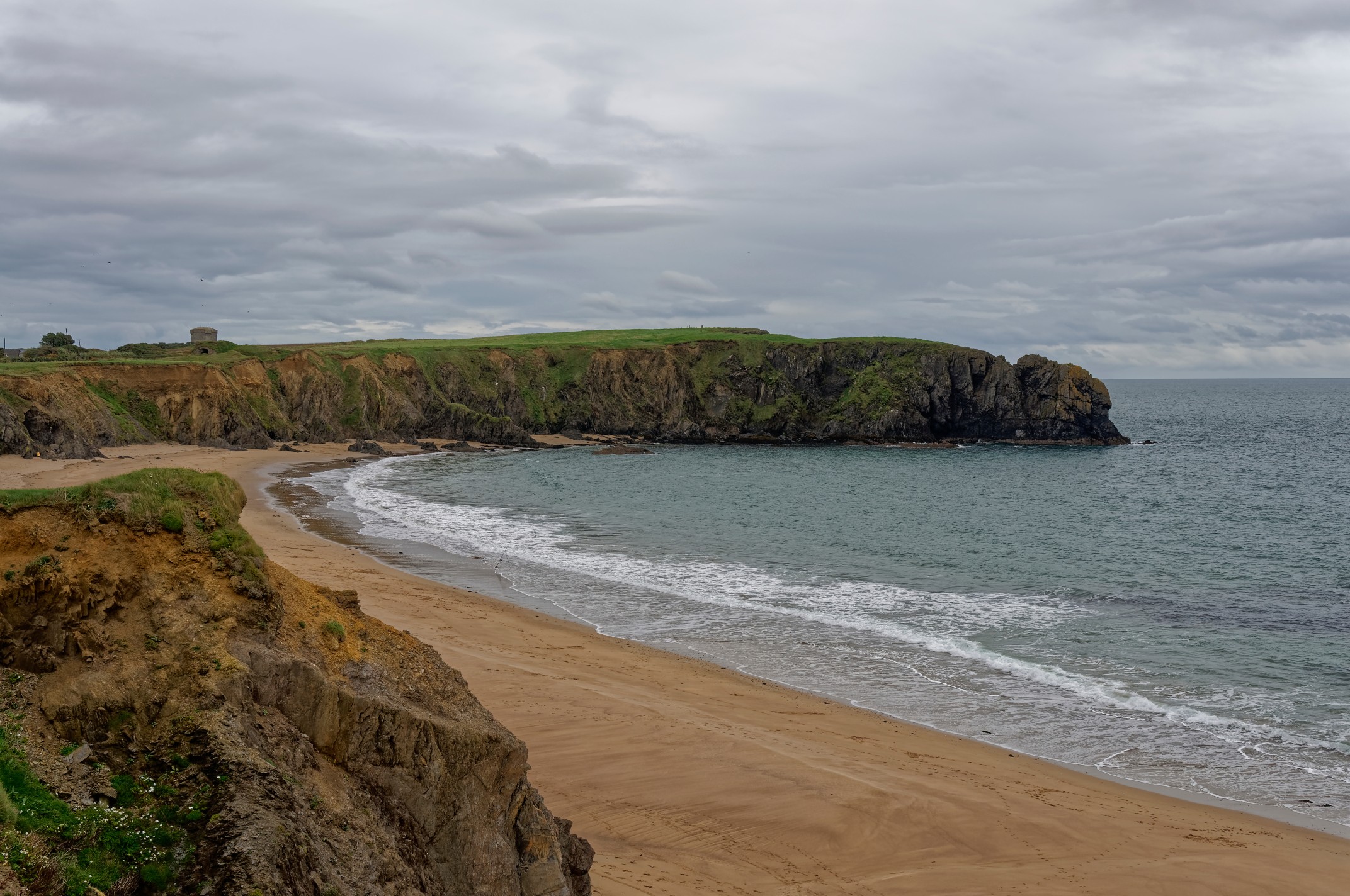 Petits Bay and Baginbun Head on an overcast day in October with the Tide going out and overlooked by a Martello Tower.
