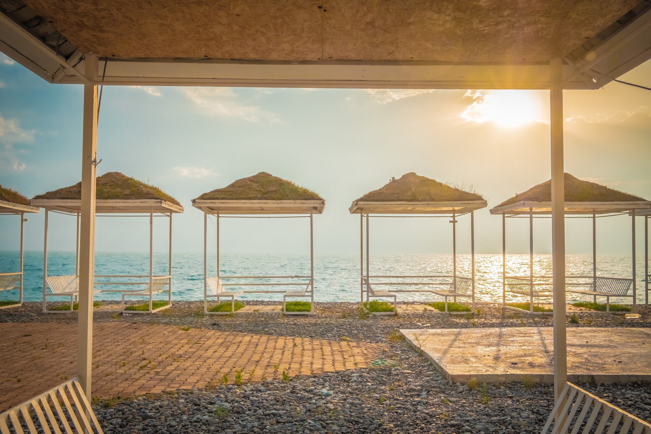 Empty summer cafe on the beach. No visitors due to pandemic and covid-19. Tables on a canopy, wooden flooring. Restaurant with sea view on the coastline. Closed borders, lack of tourists. Evening. Sun
