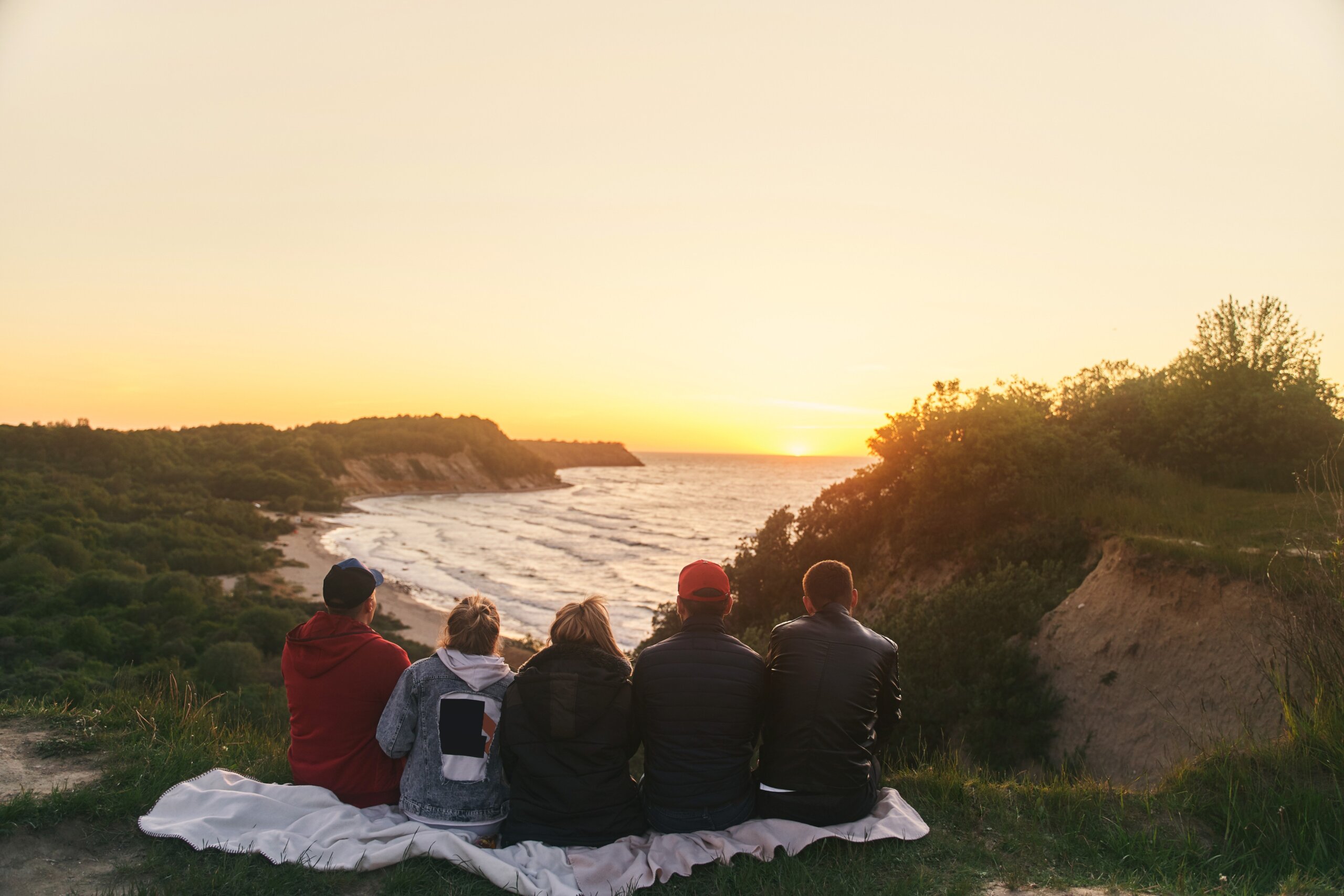 Four friends sitting on a blanket overlooking the ocean at sunset