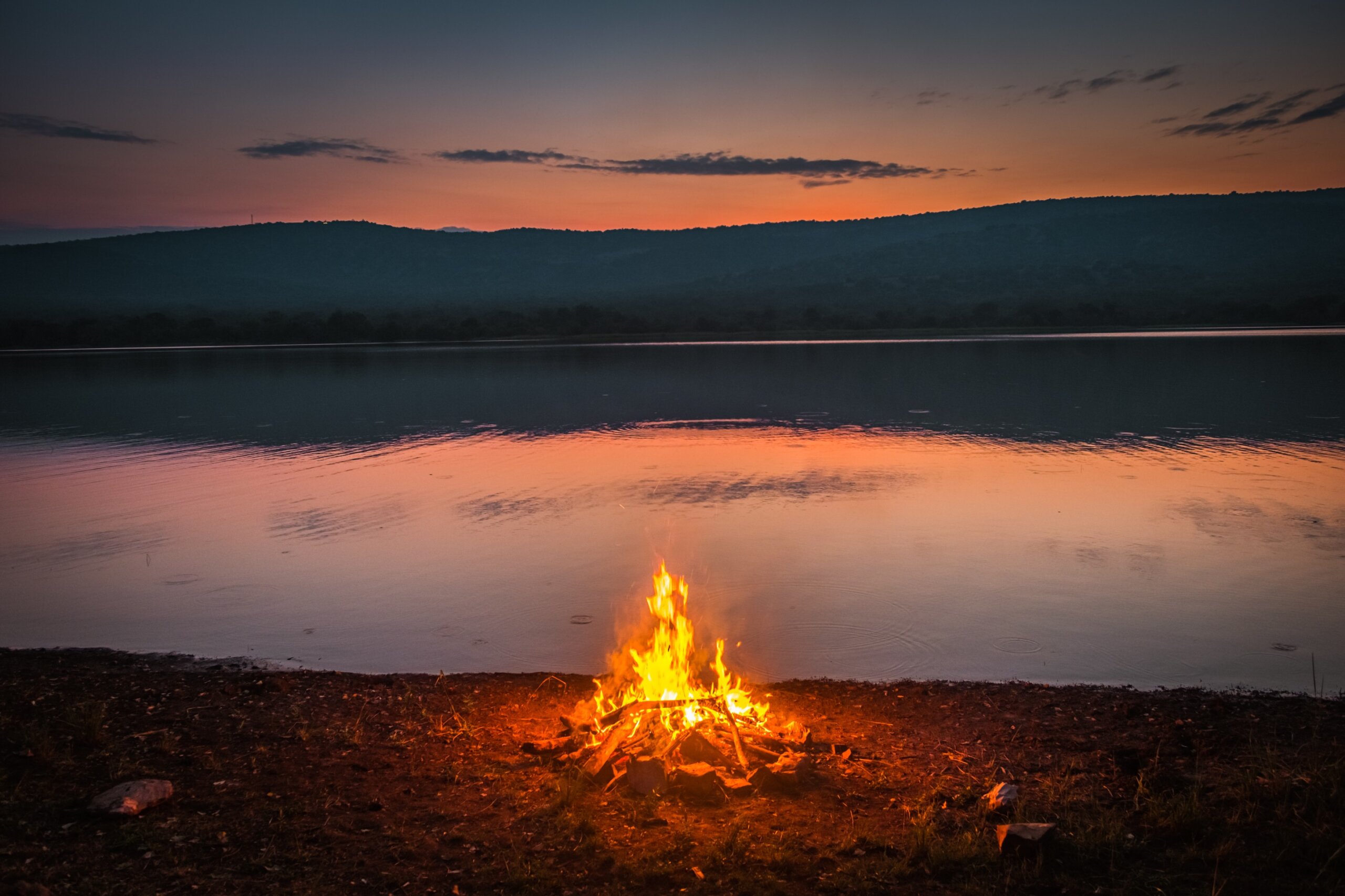 Campfire by lake at sunset representing National Geographic’s Best of the World 2026 travel destinations