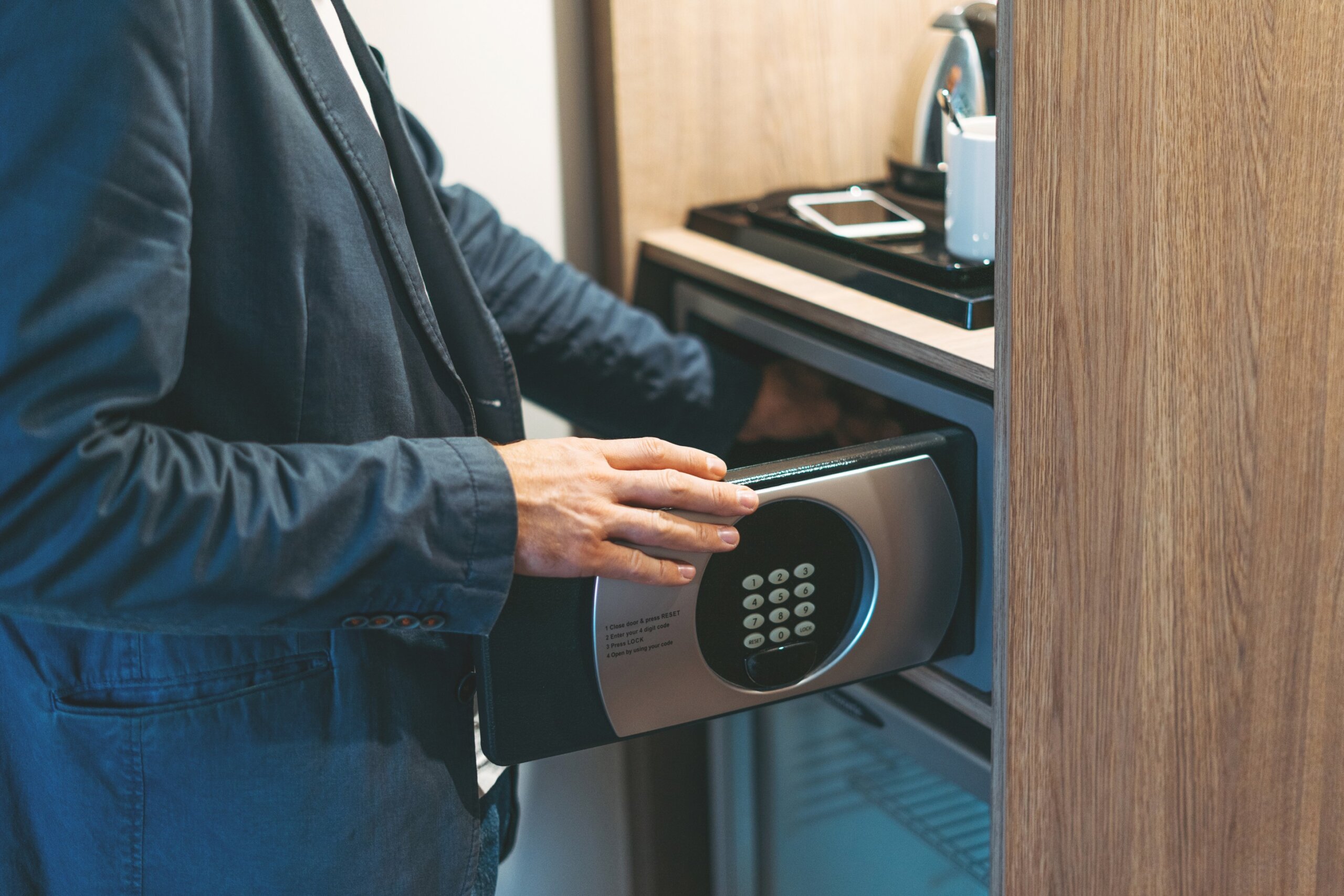 Adult man in blue jacket uses safe in the hotel room
