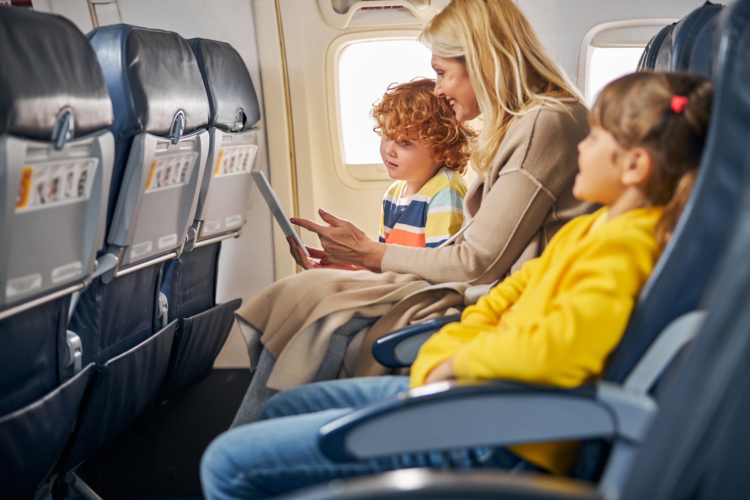 Woman inside a plane showing a tablet to a boy
