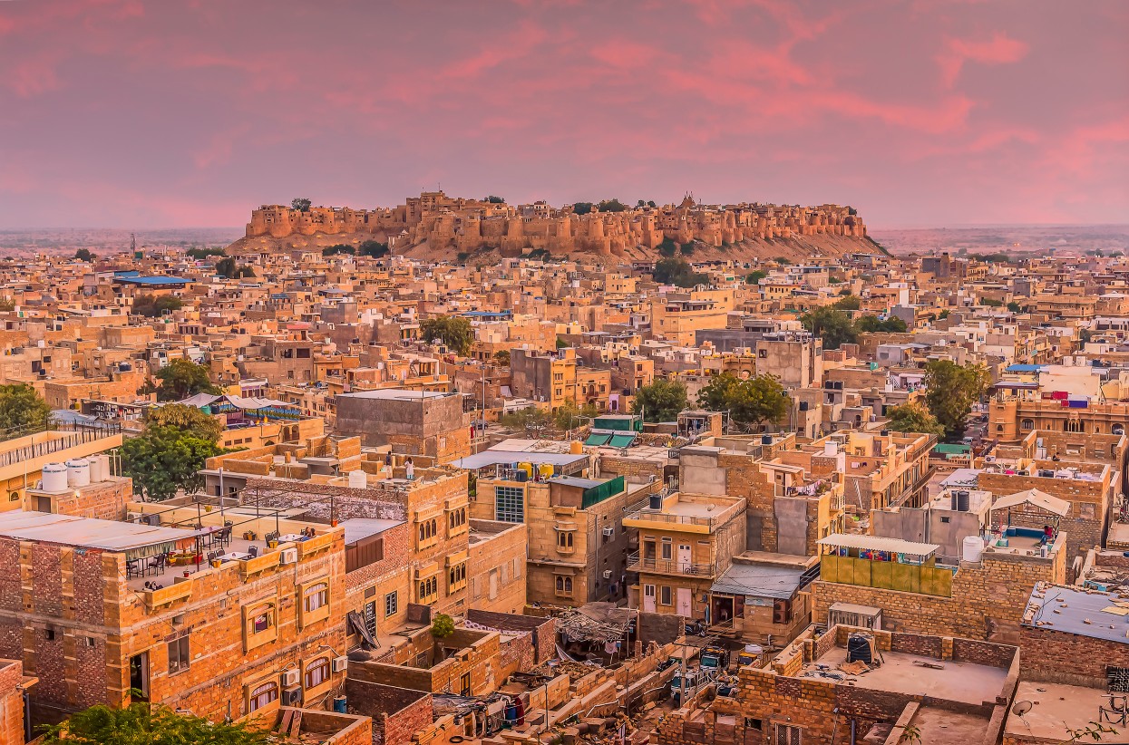 Golden city of Jaisalmer glowing at sunset in Rajasthan, India, with historic fort and sandstone buildings.