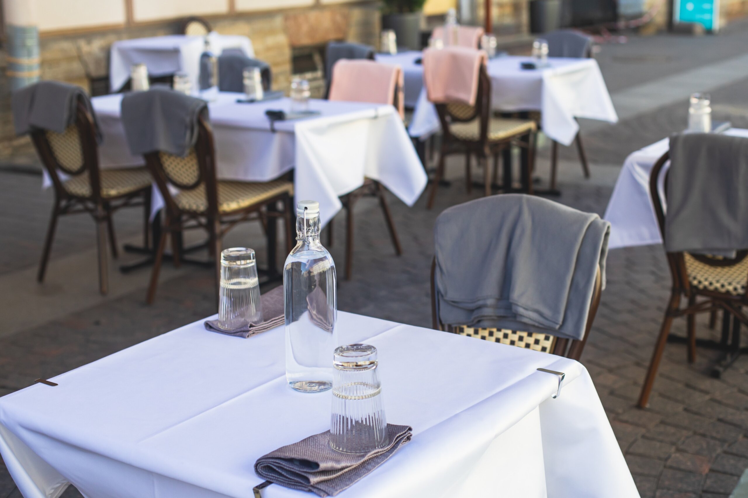 View of empty street cafe restaurant outdoor terrace veranda decoration on pedestrian european street, with chairs, tables decorated with white tablecoth, pink and grey blanket, bottles of water 