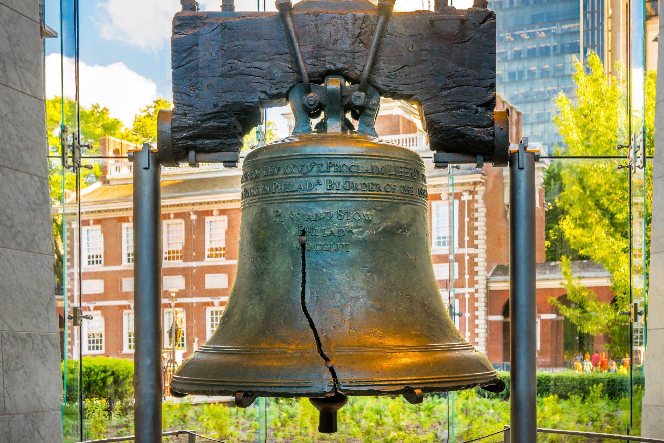 Philadelphia, Pennsylvania, USA - June 30, 2016: Liberty Bell in the Liberty Bell Center in Independence National Historical Park with sunlit Independence Hall in the background. 