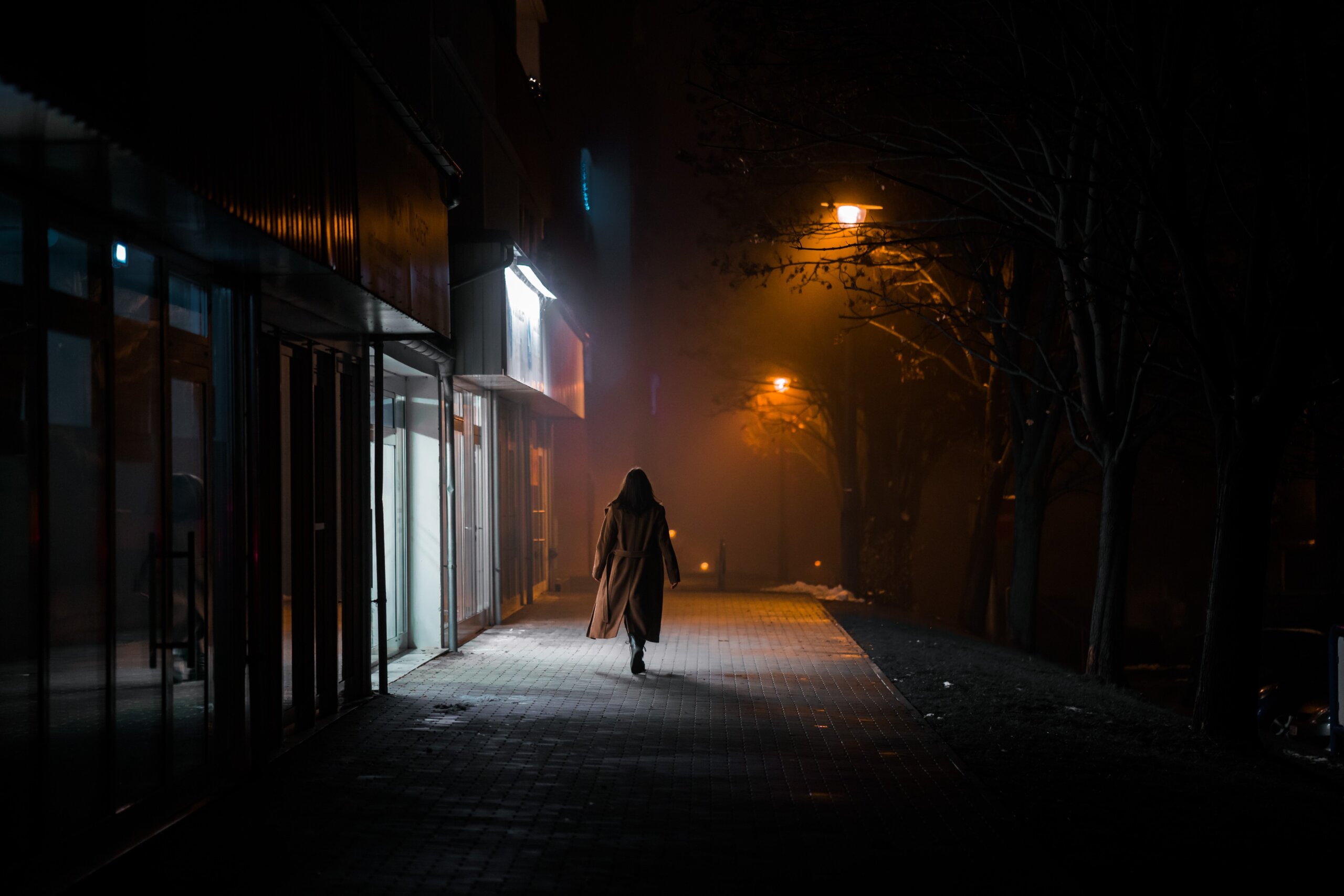 dark silhouette of a girl dressed in a long coat against the background of a night city with advertising showcases