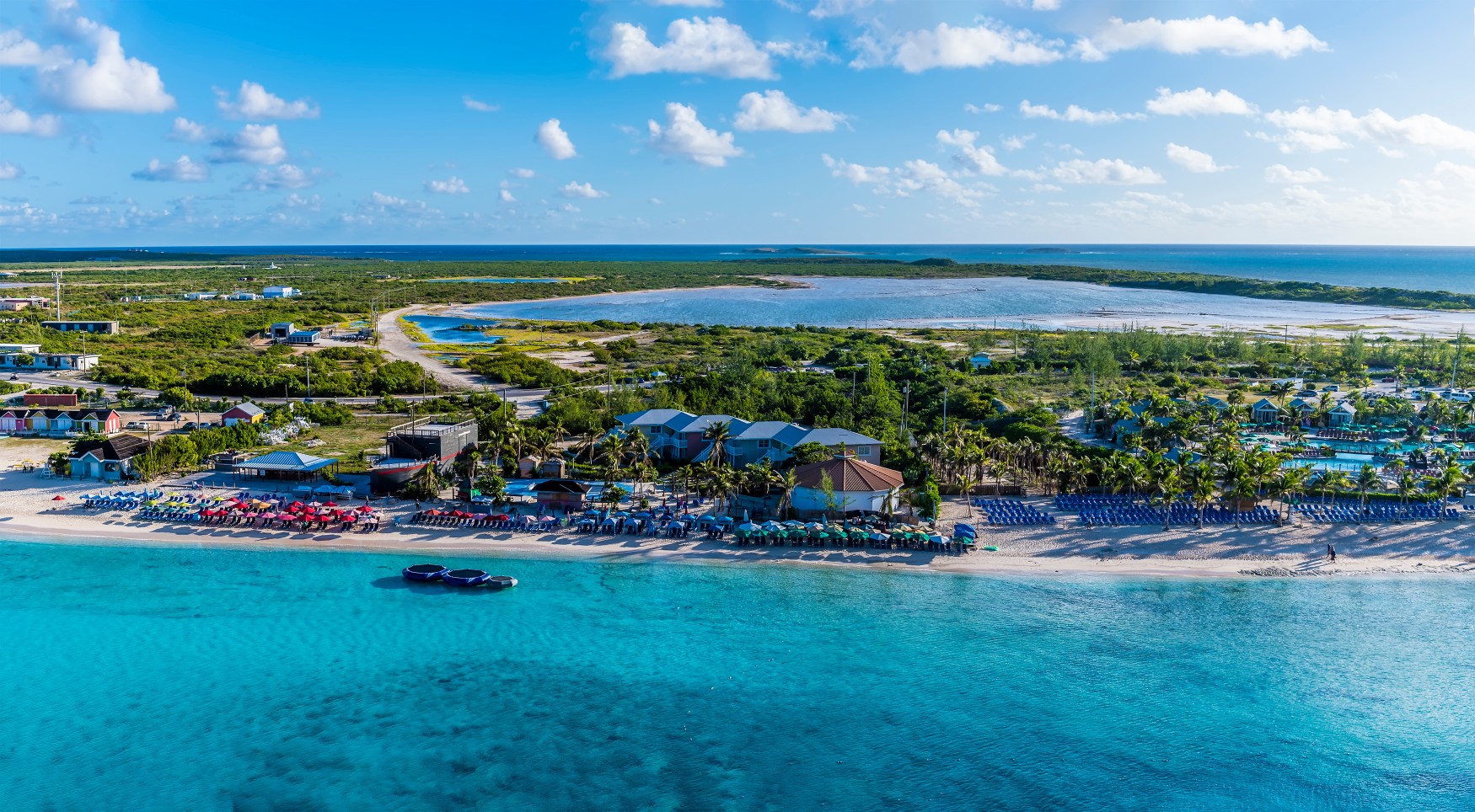 Aerial view of Grand Turk beach and resorts in Turks and Caicos with turquoise water and colorful umbrellas.