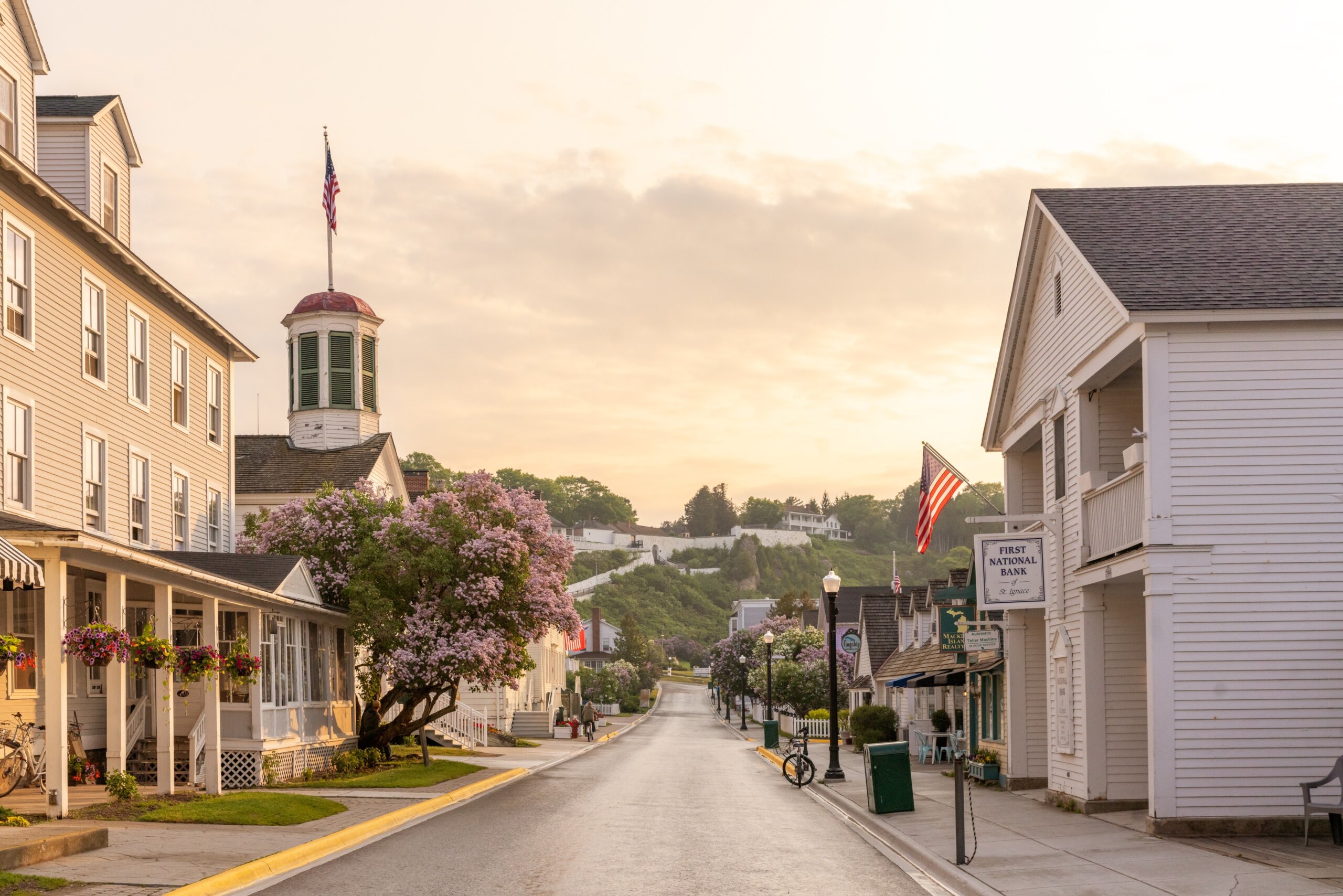 Street at dawn on Mackinac Island during the Lilac Festival, with historic buildings and American flags.