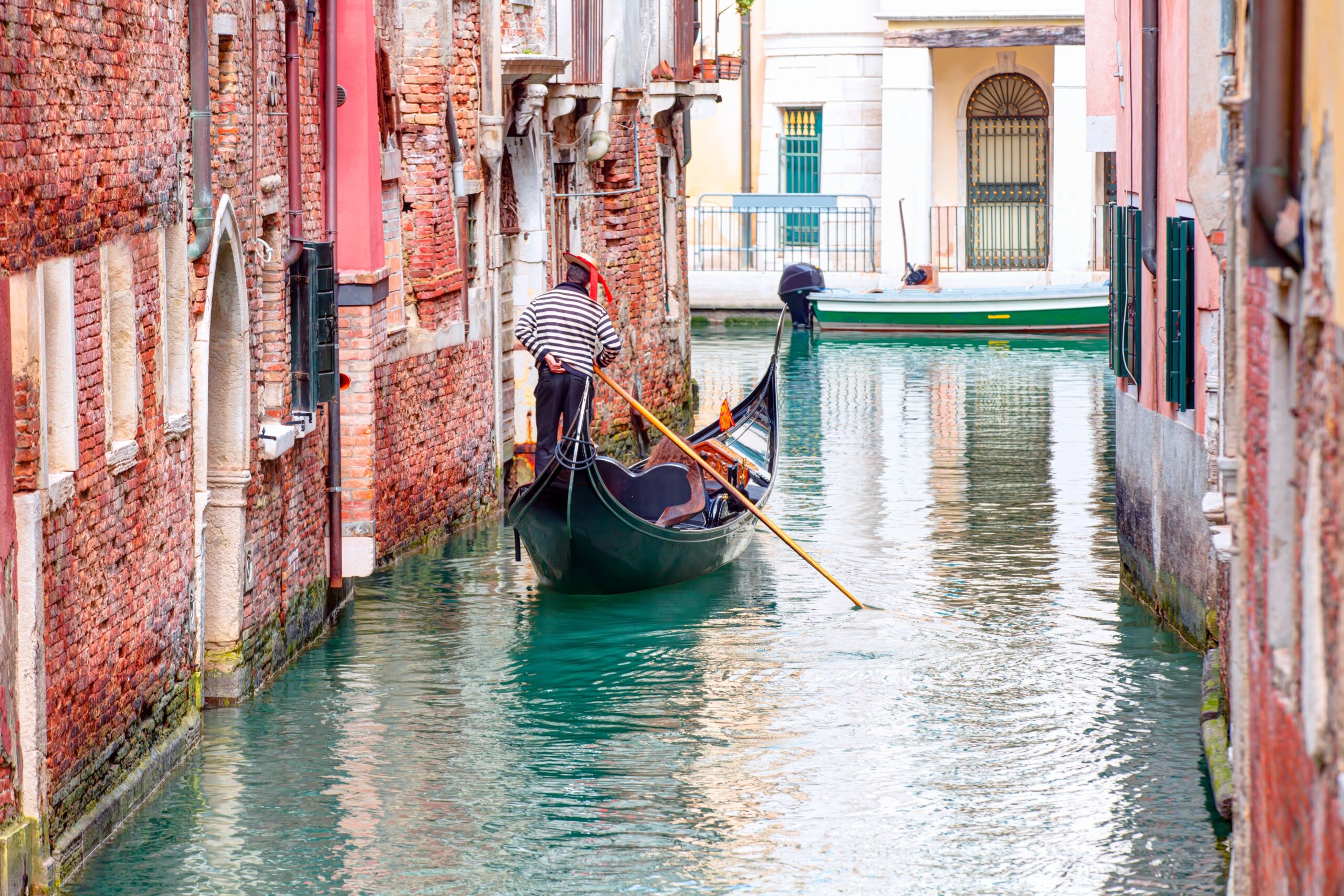 Venetian gondolier punting gondola through green canal waters of Venice Italy
