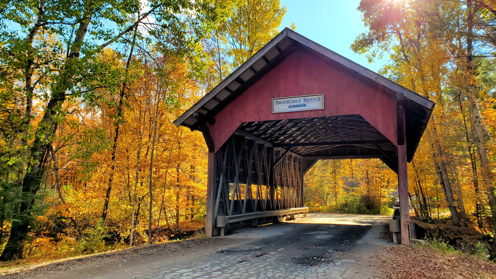 Red wooden Brookdale Bridge surrounded by bright autumn trees in Stowe, Vermont, USA.