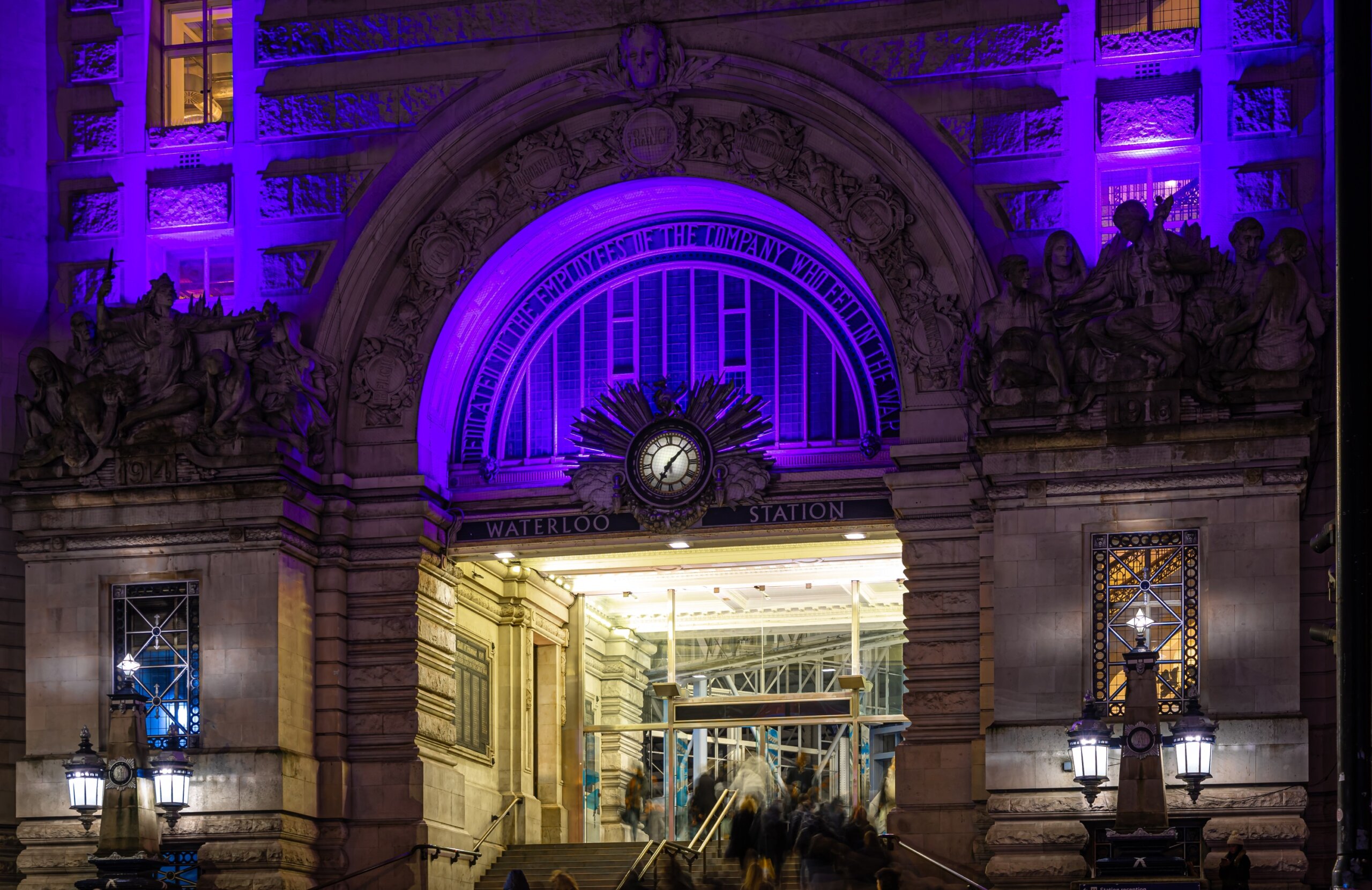 Exterior of London Waterloo Station at night with purple lights, representing U.K. Christmas travel disruptions and holiday train schedules.