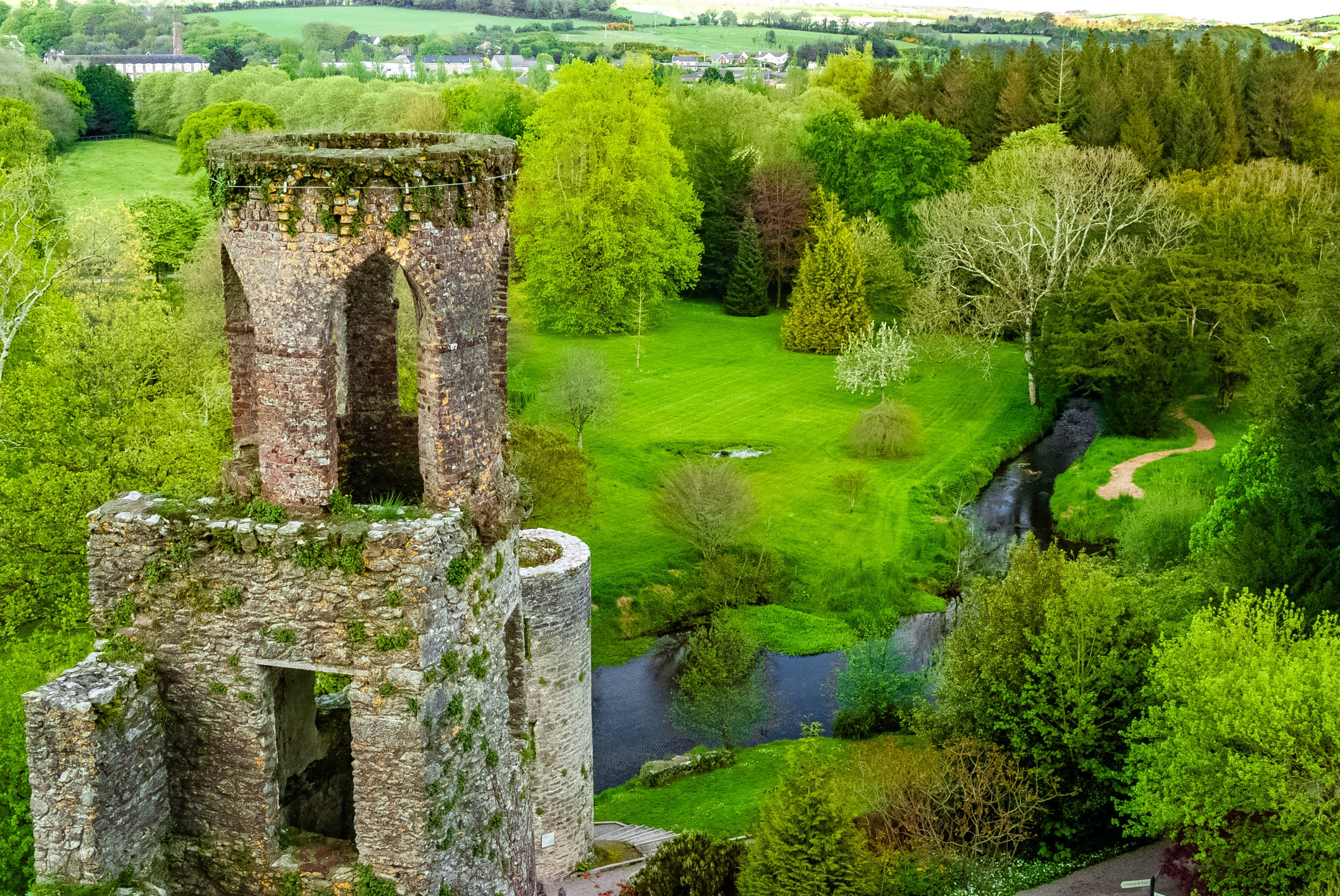 Blarney Castle in County Cork, Ireland, surrounded by green hills and trees after a spring rain.
