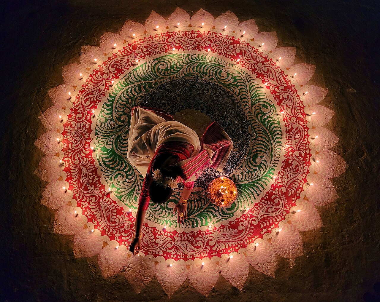 Overhead shot of woman decorating a rangoli with oil lamps for Diwali in India.