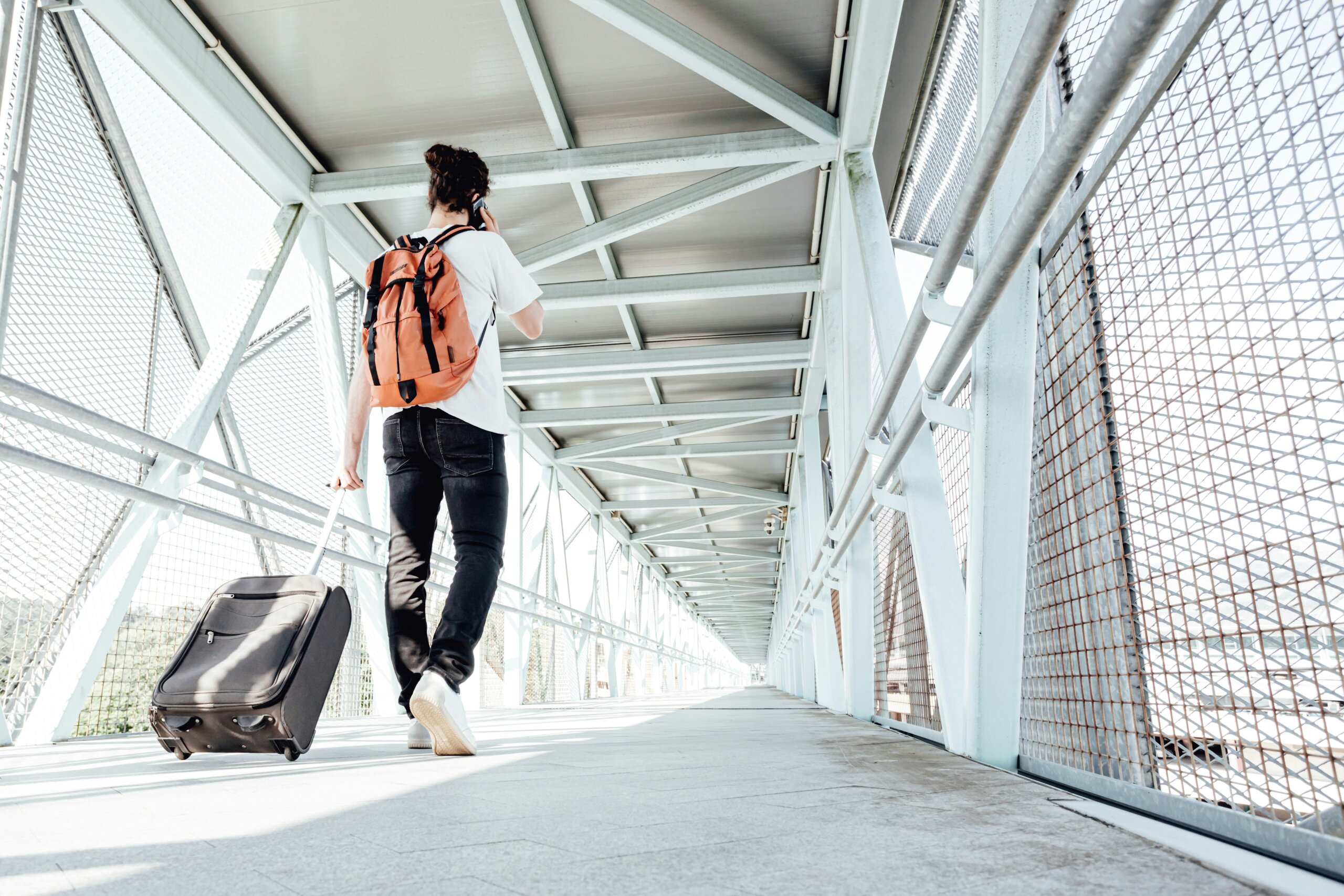 Traveler with a backpack and suitcase walking through an airport bridge, representing flexible and adaptable travel habits.