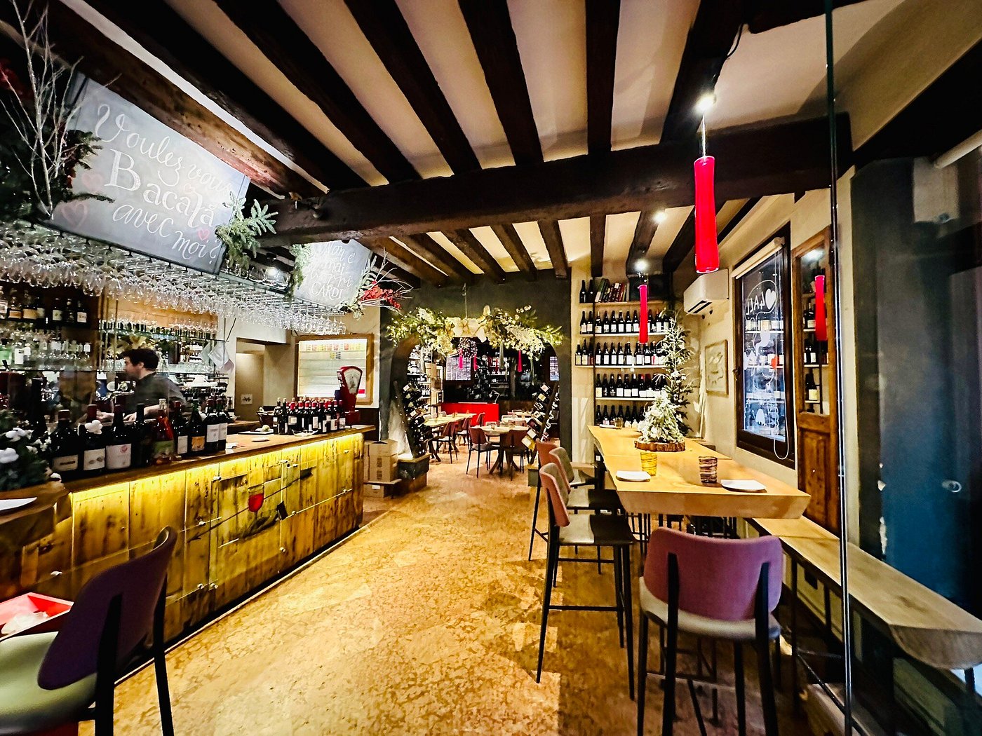 Warm interior of Estro wine bar and kitchen in Dorsoduro, Venice, with wooden beams, wine shelves, and cozy dining tables.