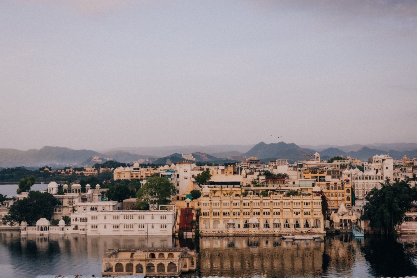 Panoramic view of Udaipur’s City Palace and Lake Pichola reflecting golden buildings at sunset in Rajasthan, India.