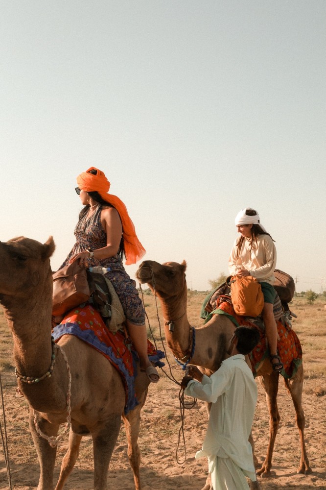 Travelers riding camels in Rajasthan desert guided by a local man during an India travel adventure.