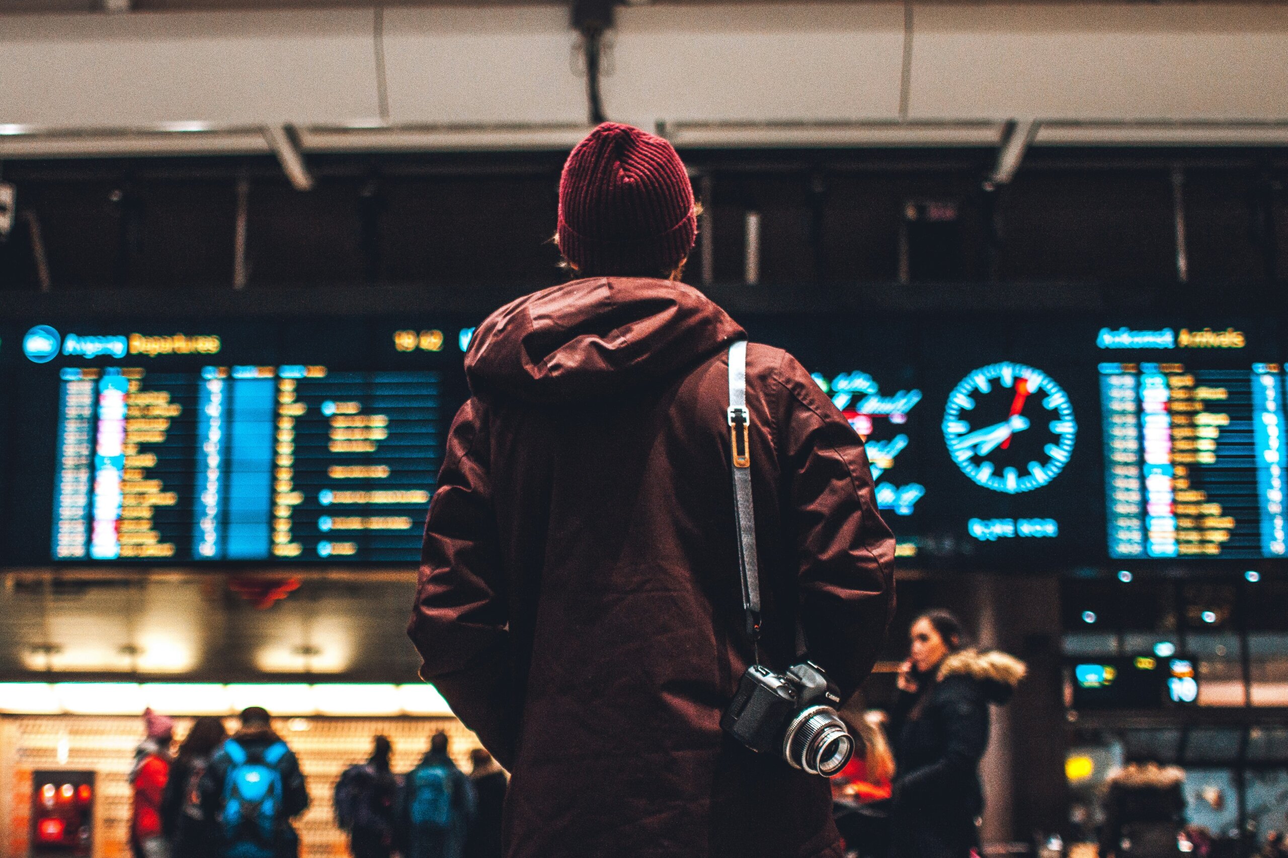 Young traveler at an airport terminal checking flight information board, representing spontaneous last-minute travel choices.