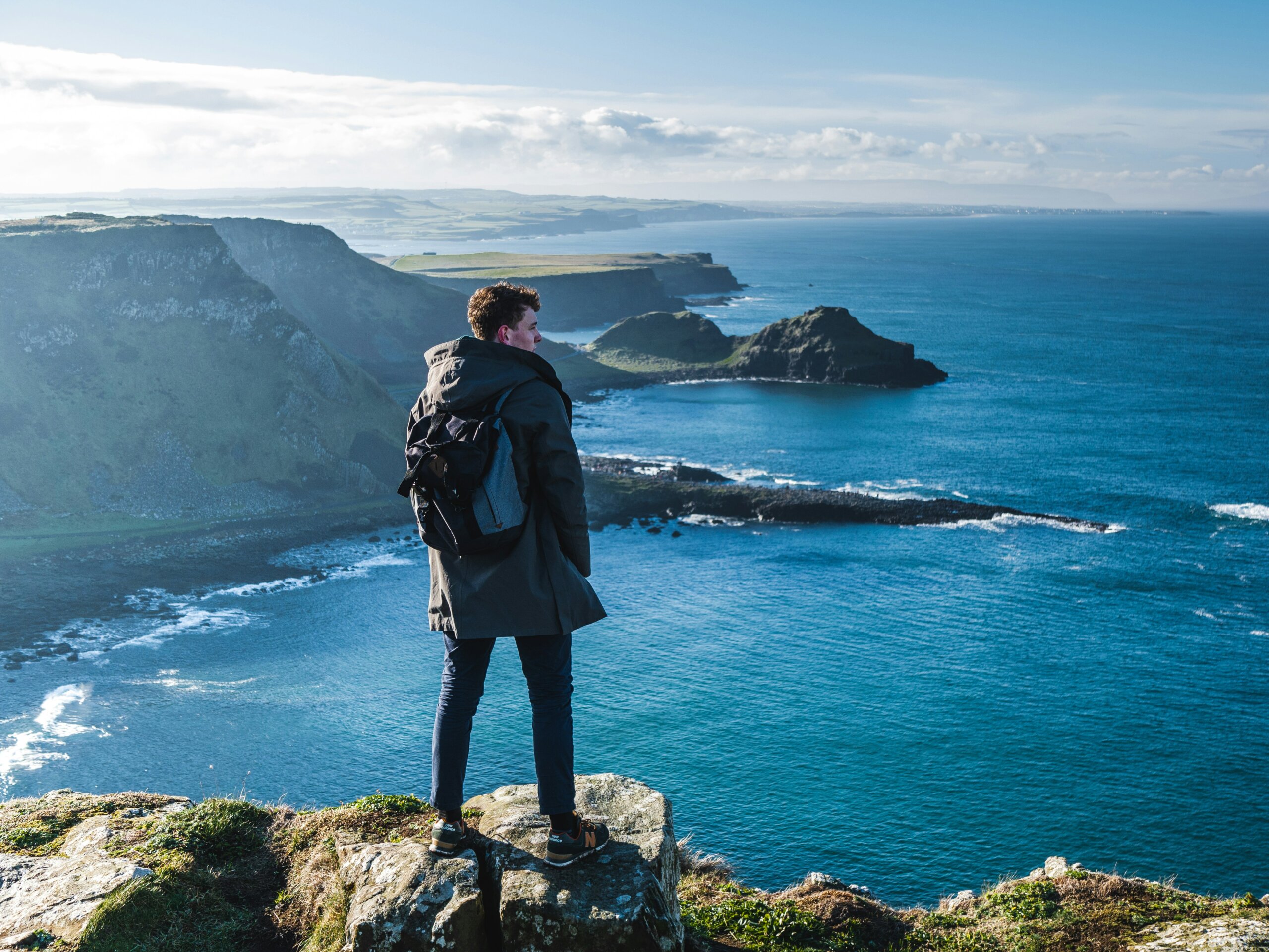 Traveler standing on a cliff overlooking Ireland’s winter coastline with blue sea and rugged cliffs.