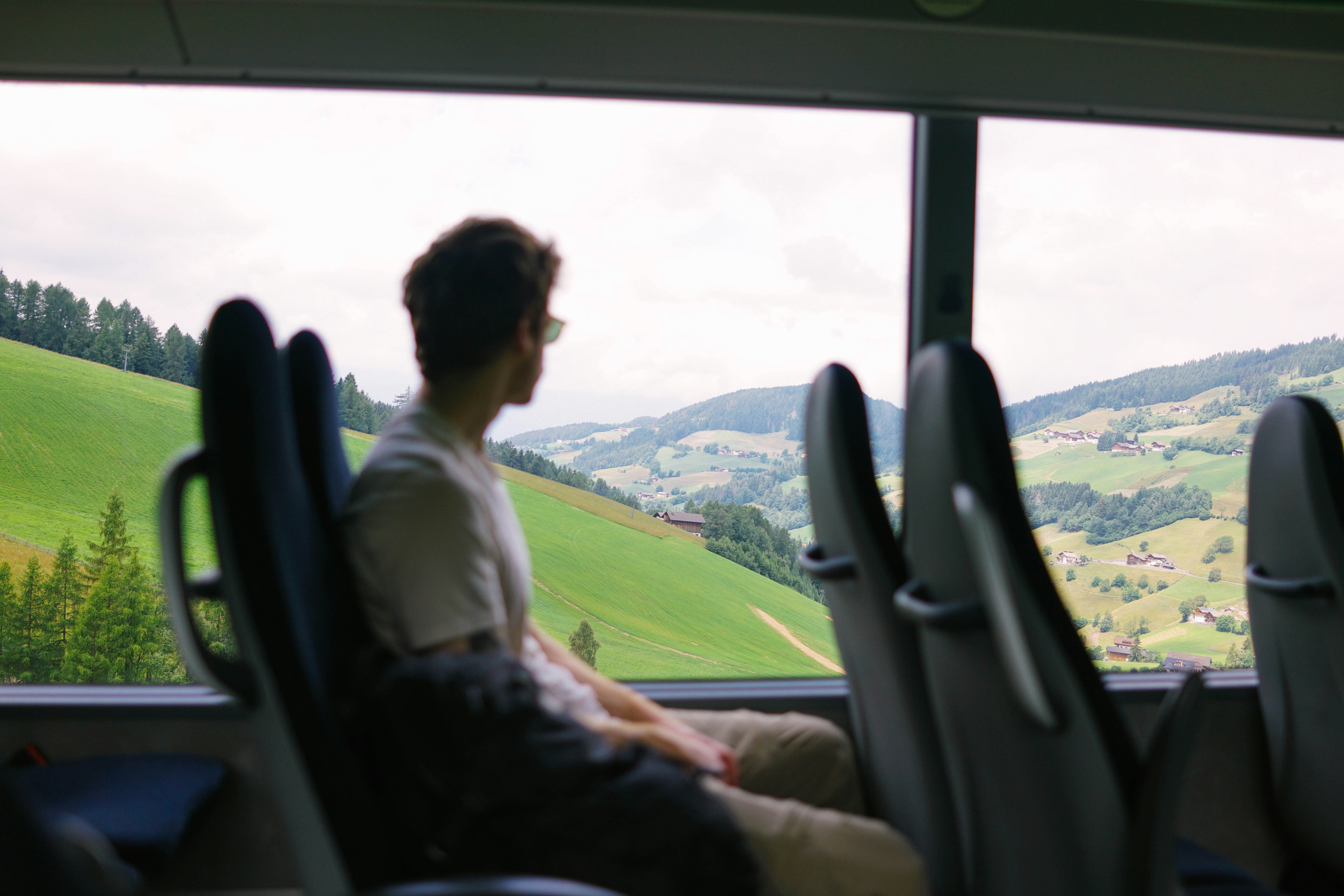 Traveler on a bus looking out at green countryside, highlighting eco-friendly and budget-conscious travel choices.
