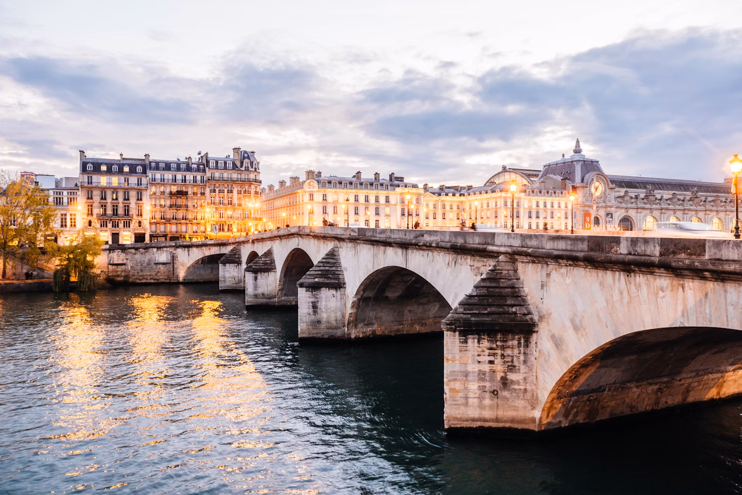 Pont Neuf bridge in Paris glowing at sunset with Seine River reflections, symbolizing the real Paris beyond tourist crowds.