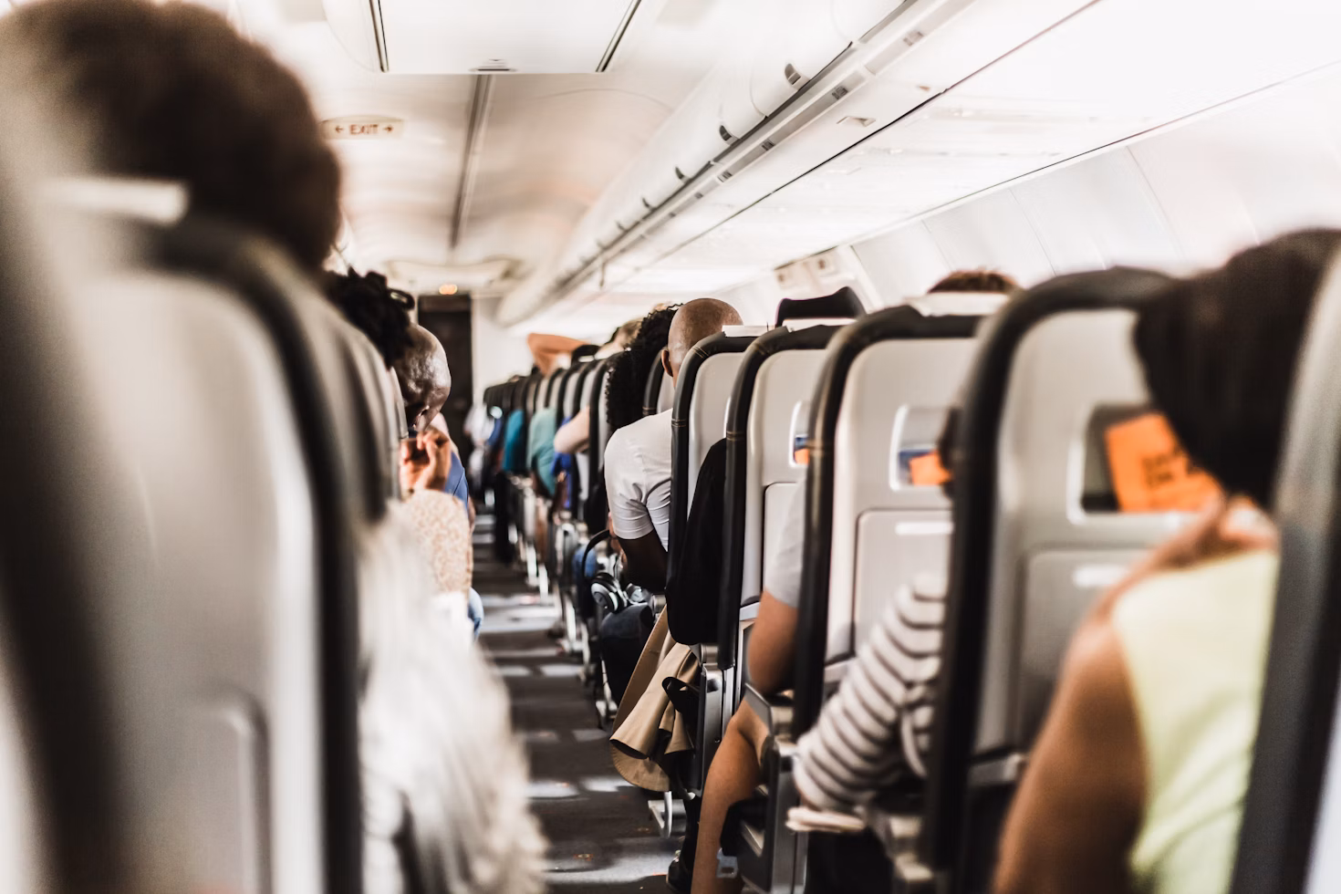 Passengers seated on airplane flight viewed from behind showing crowded cabin and travel etiquette scene.