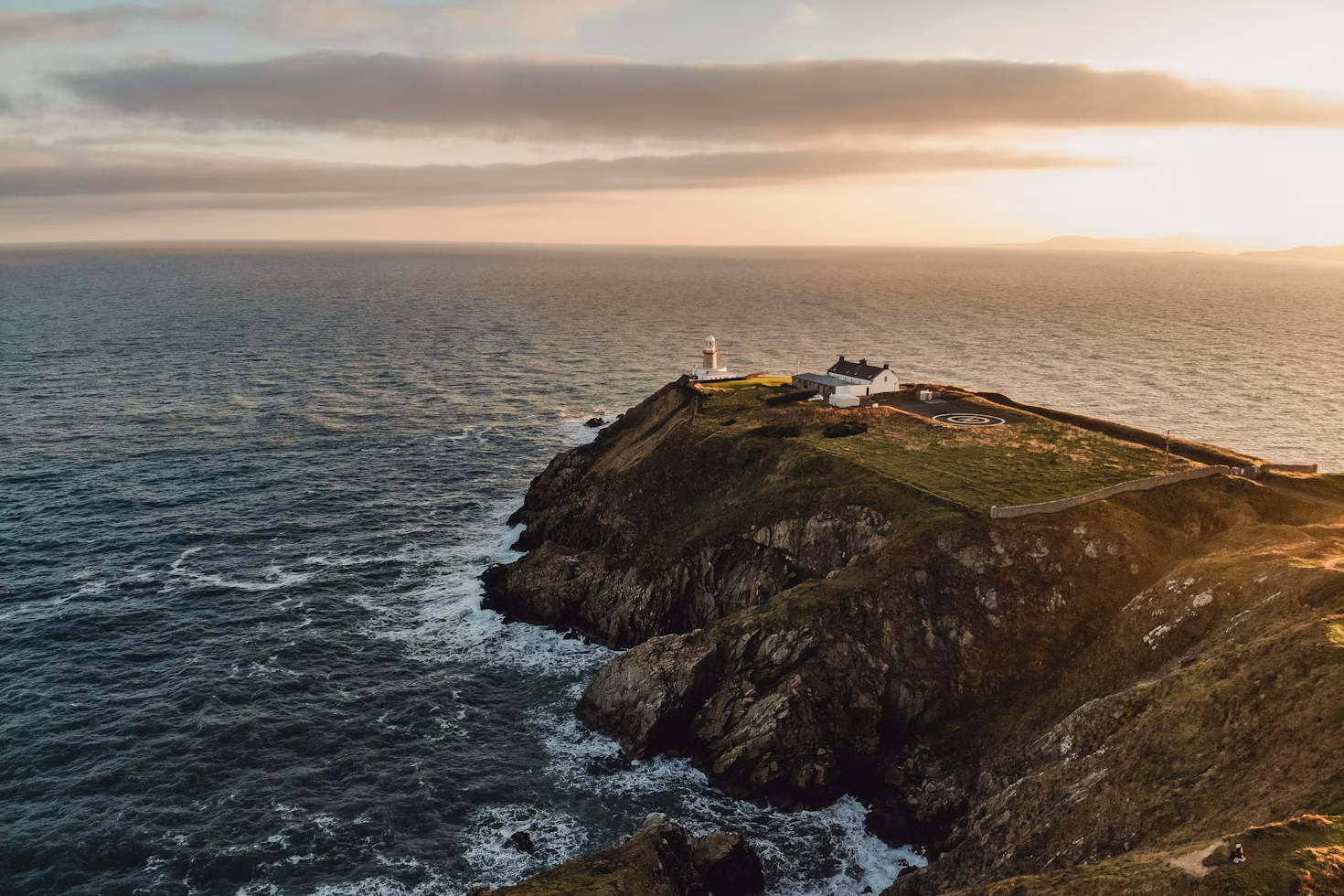 house and lighthouse at the edge of island cliff - beach, sea, and sunset in Dublin, Ireland