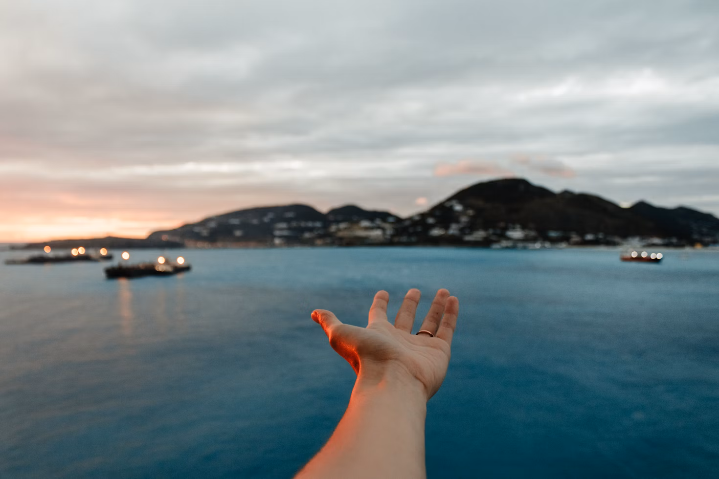Traveler’s hand reaching over the ocean from a cruise ship deck at sunset, symbolizing the best cruise experiences for every kind of traveler.