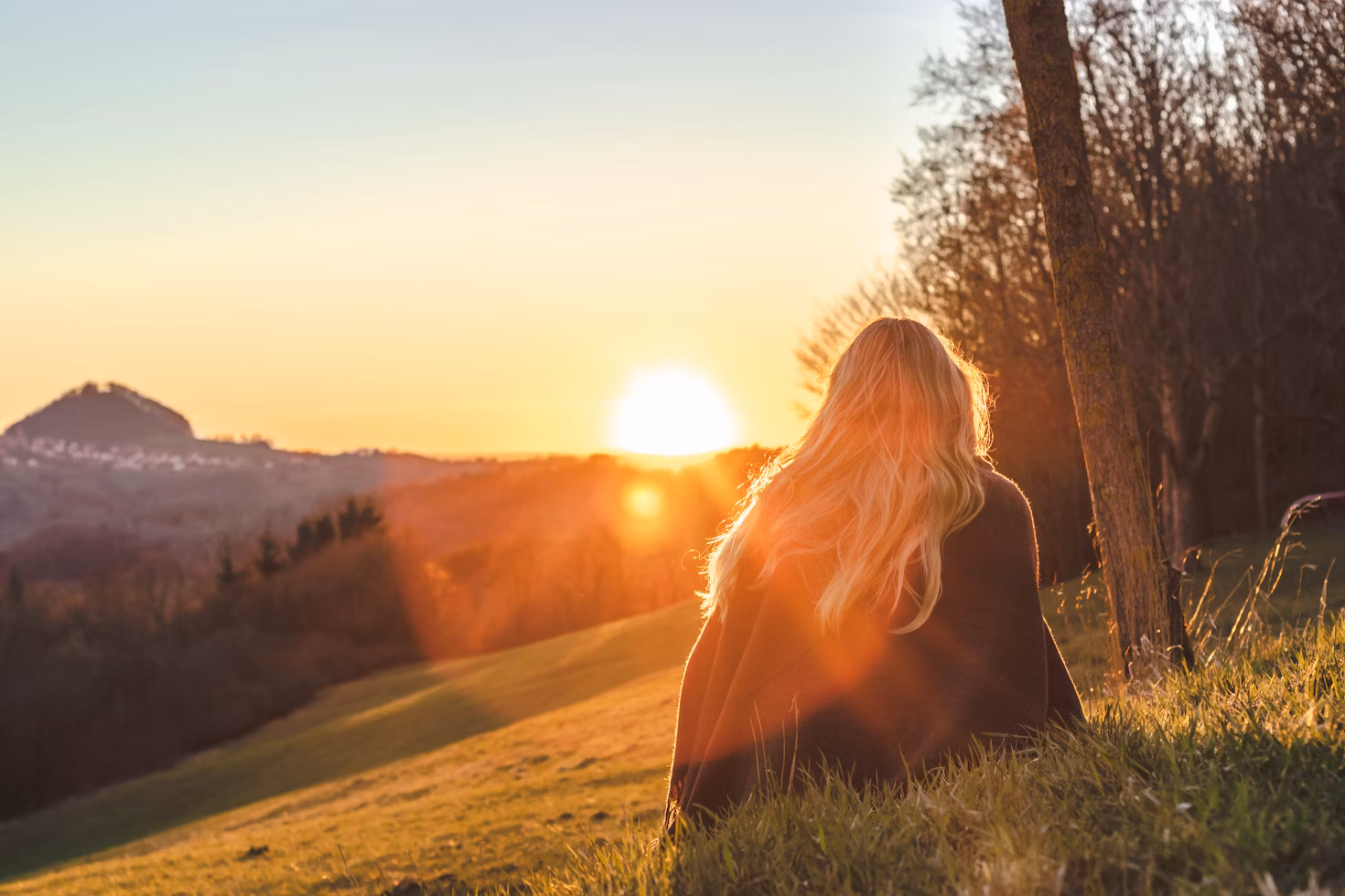 Woman sitting on a hillside at sunset, symbolizing the essence of slow travel and mindful journeys.
