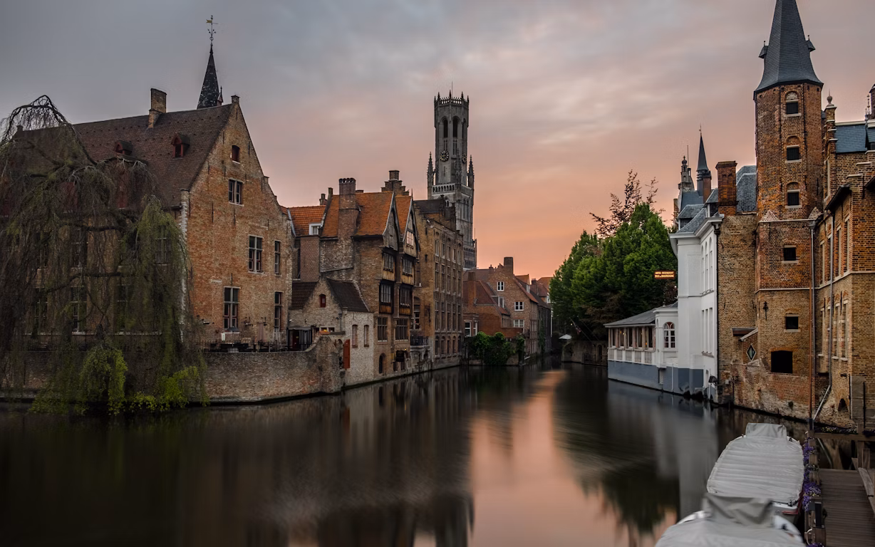 brown concrete buildings beside calm body of water. HD photo of building, architecture, river, and urban in Bruges, Belgium by Elijah G (@elijjah)