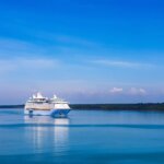 Luxury cruise ship sailing on calm blue sea under clear sky, symbolizing all-inclusive travel and relaxation.
