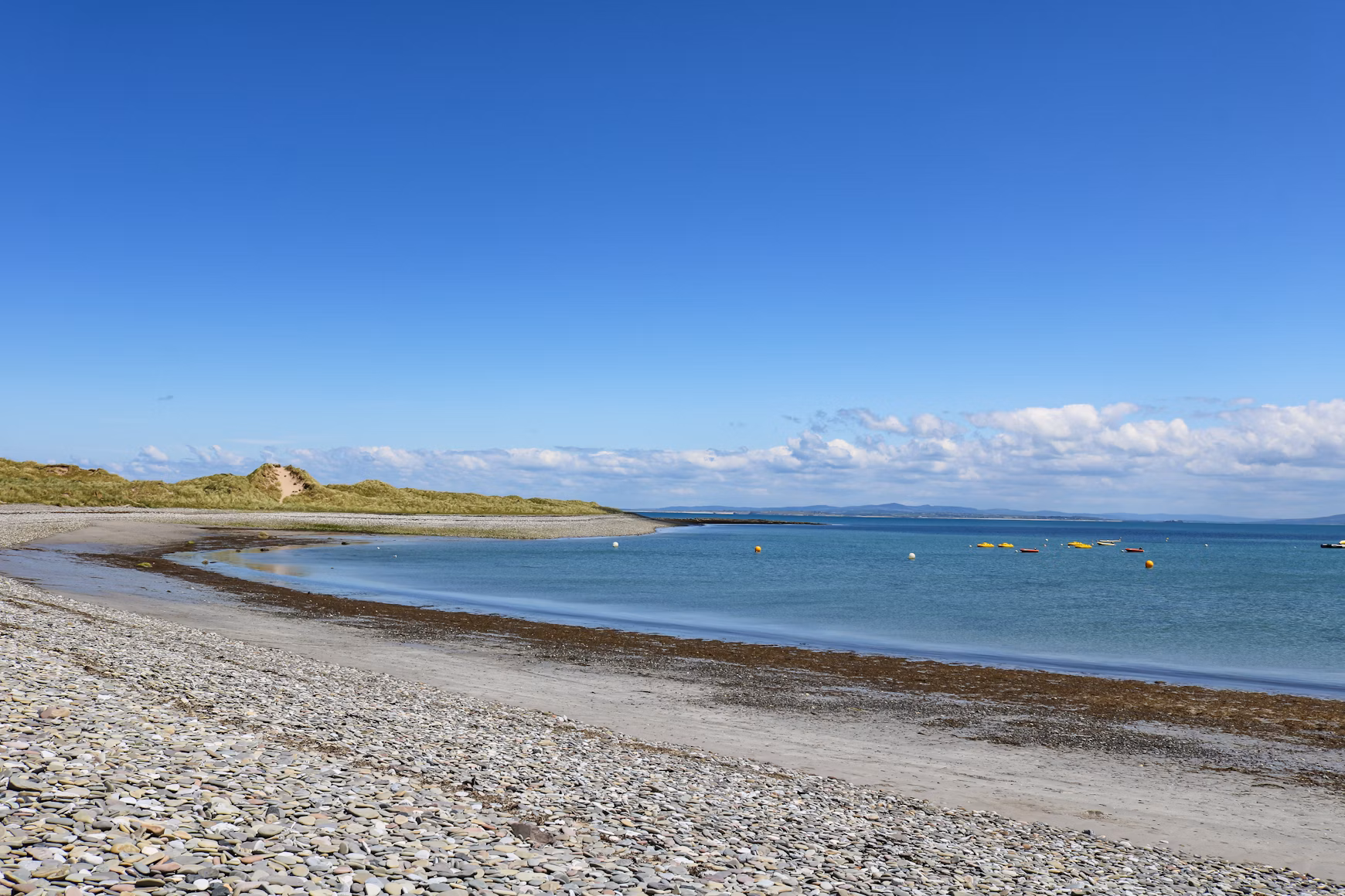 Peaceful Irish beach with pebbled shore, calm blue sea, and clear skies on a sunny day, capturing the stillness of Ireland’s hidden coasts.