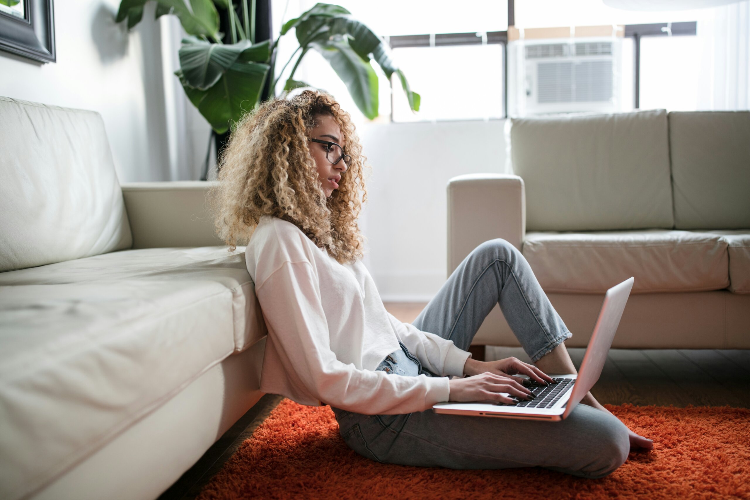 Young woman sitting on the floor with a laptop, ready to book a spontaneous trip using travel tools and alerts.