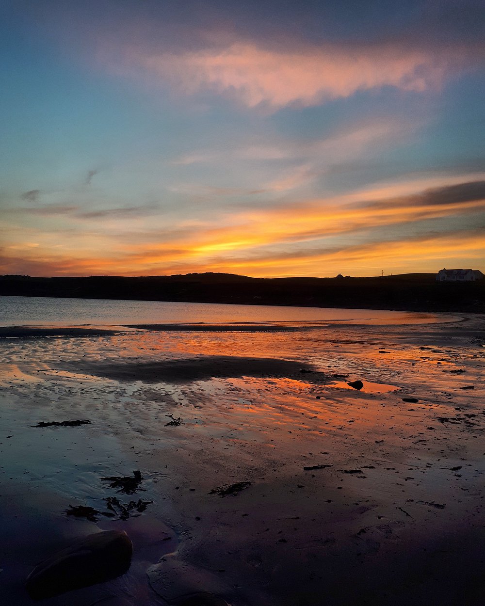 Vibrant sunset at White Strand beach in County Clare, Ireland, with orange and pink skies reflected on the wet sand and shoreline.