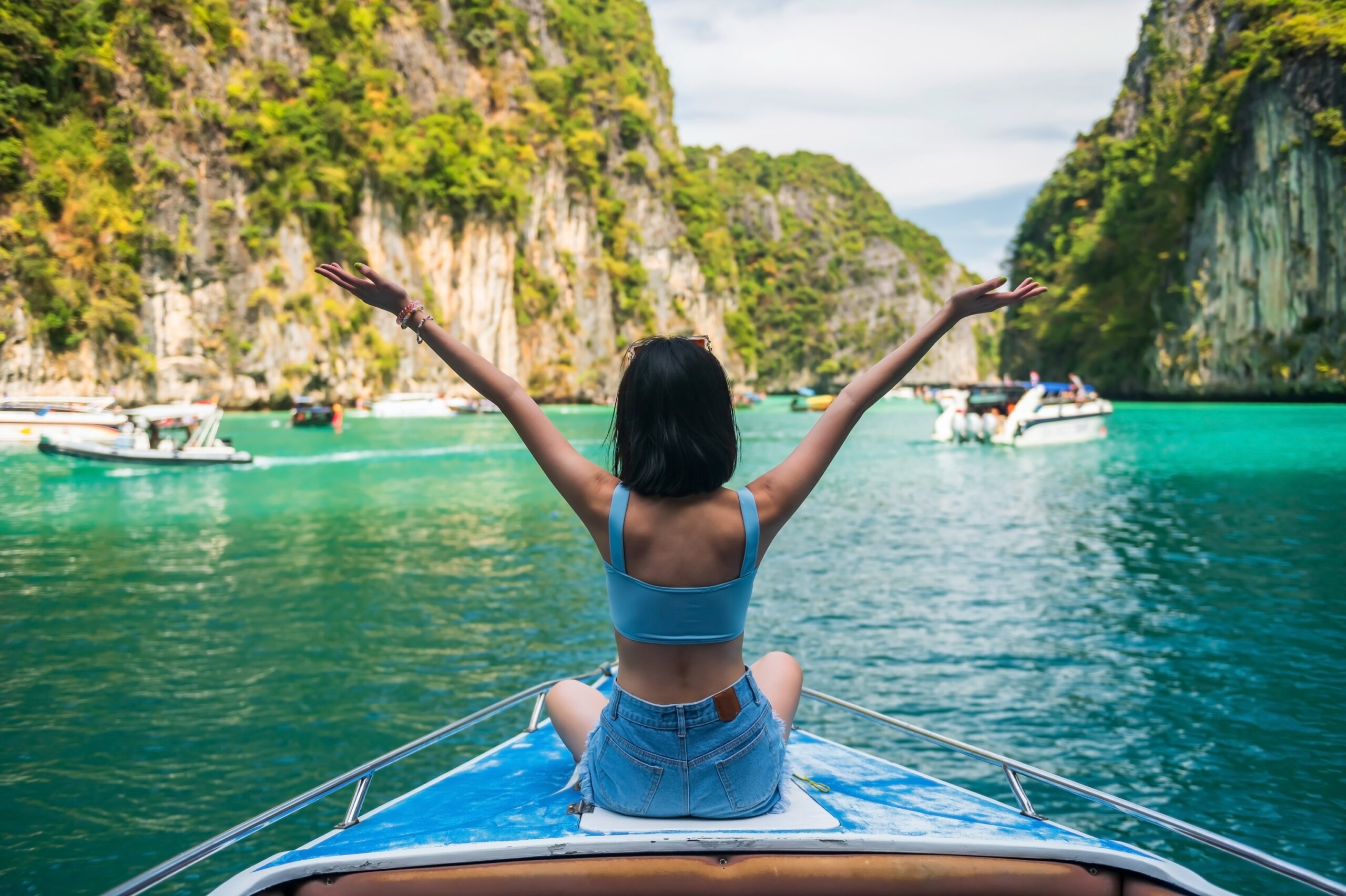 Woman on boat raising arms in turquoise lagoon surrounded by cliffs and tropical scenery