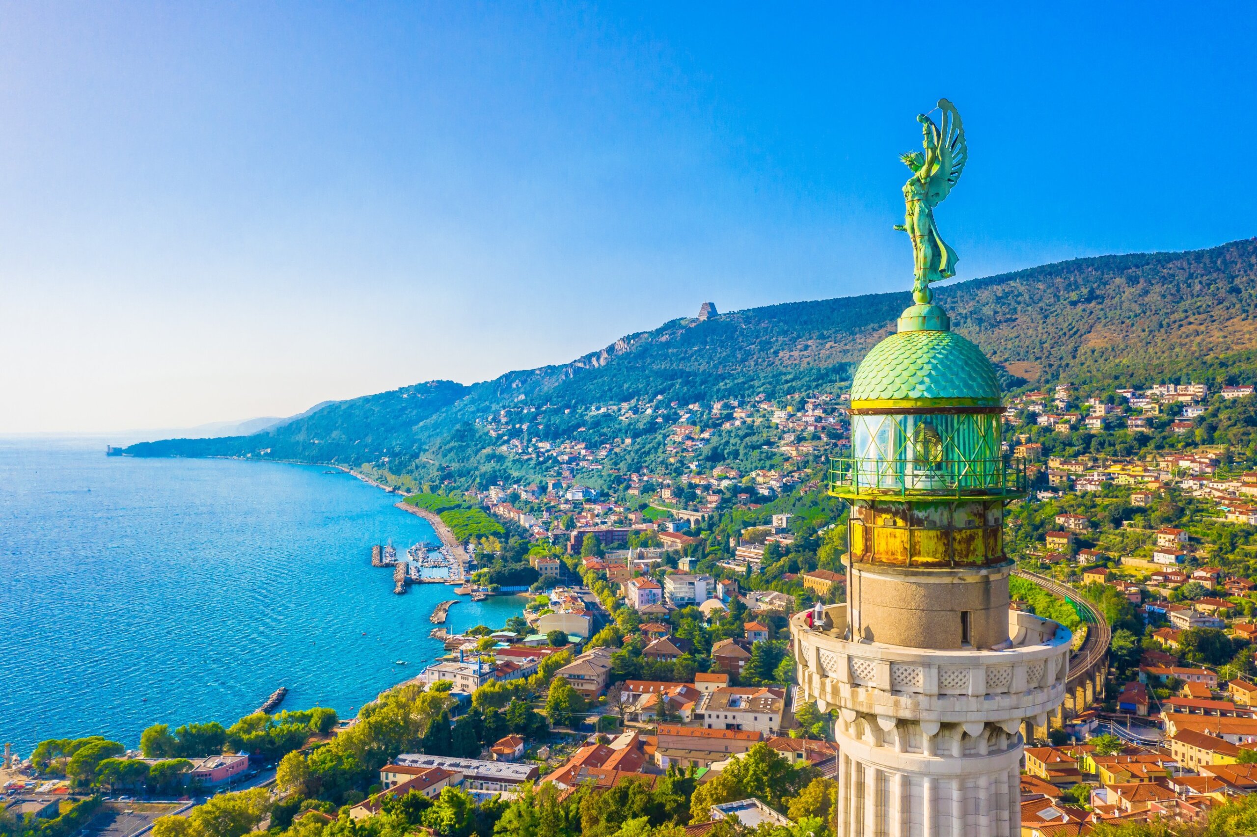 Aerial view of Trieste’s Victory Lighthouse at sunset with Adriatic Sea coastline in the background.