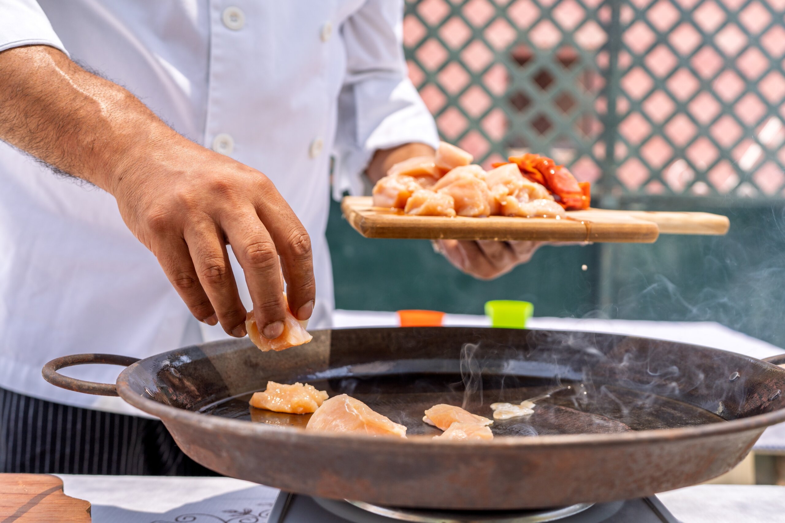 Chef adding chicken to paella pan, cooking outdoors for family meal
