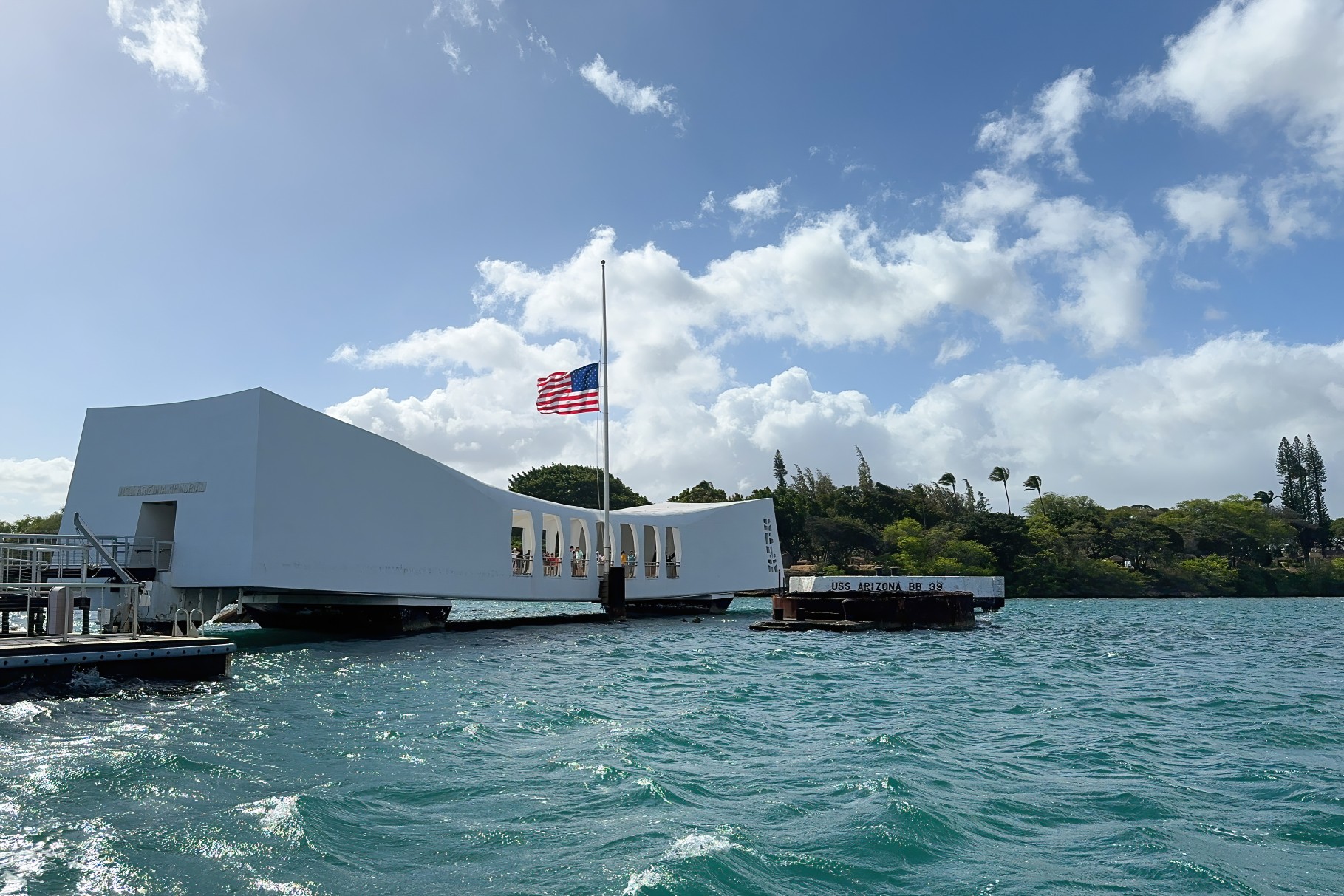Pearl Harbor, Hawaii, USA - April 4, 2024: The U.S.S. Arizona Memorial with flag of the United States at half mast against blue sky with clouds
