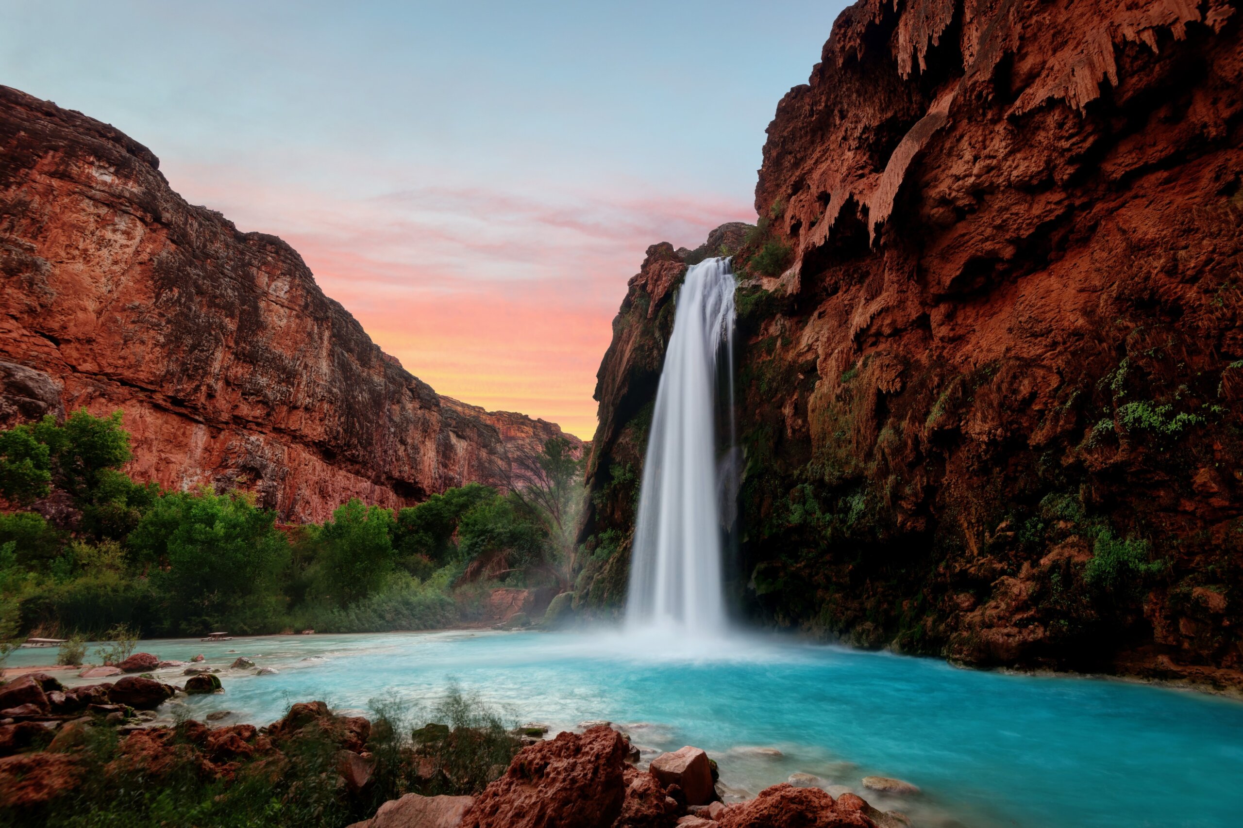 Waterfall at Havasu Falls flowing into turquoise water at sunset surrounded by red canyon cliffs