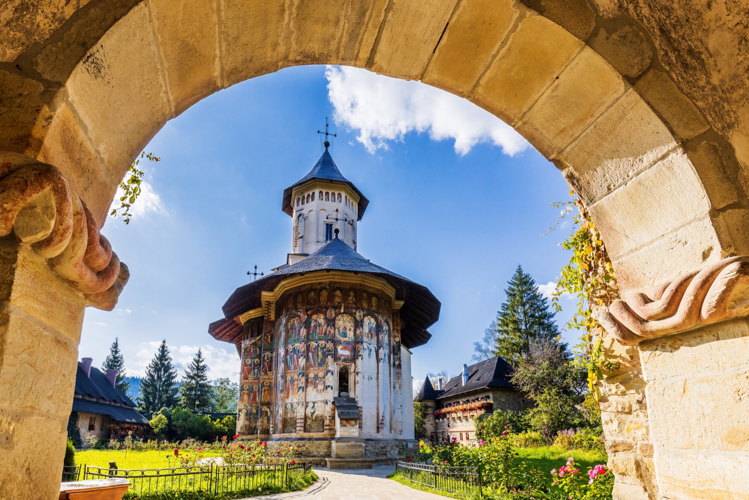 Romanian Orthodox monastery with exterior frescoes framed by an old stone archway