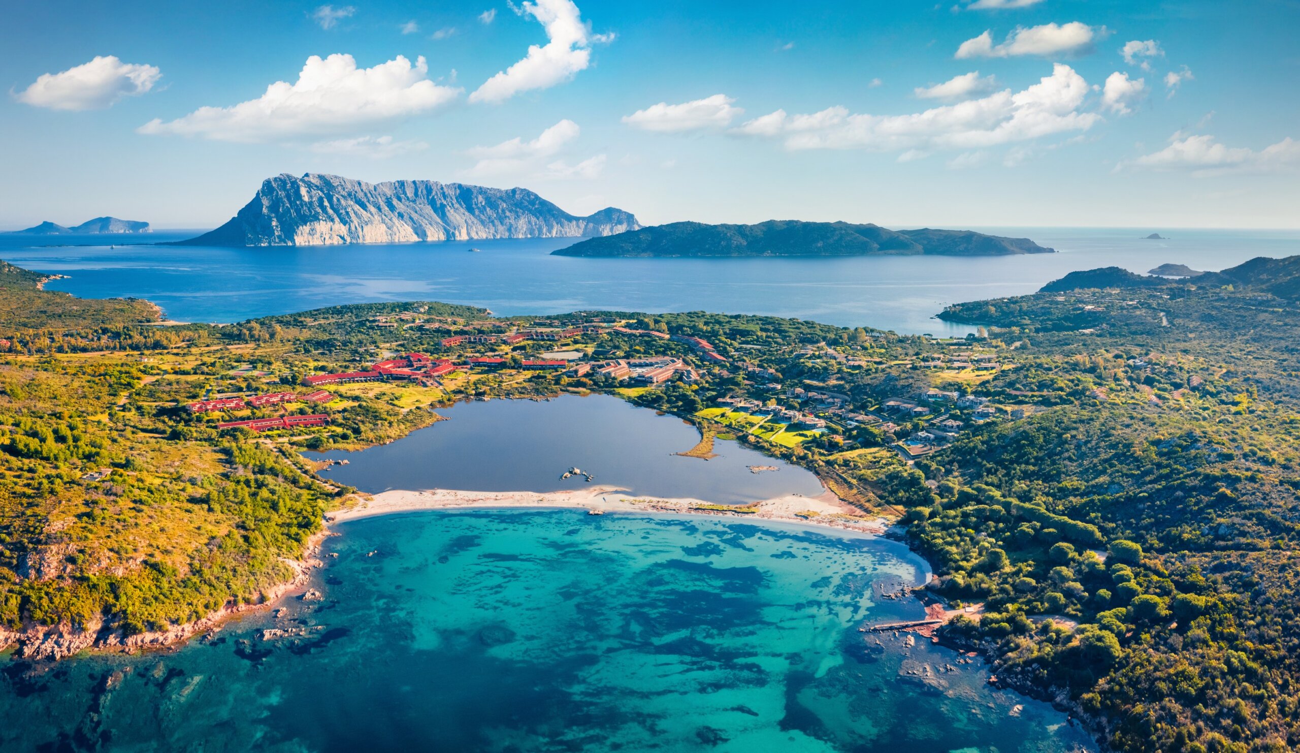 Aerial view of turquoise Mediterranean bay with lush coastline and distant islands.