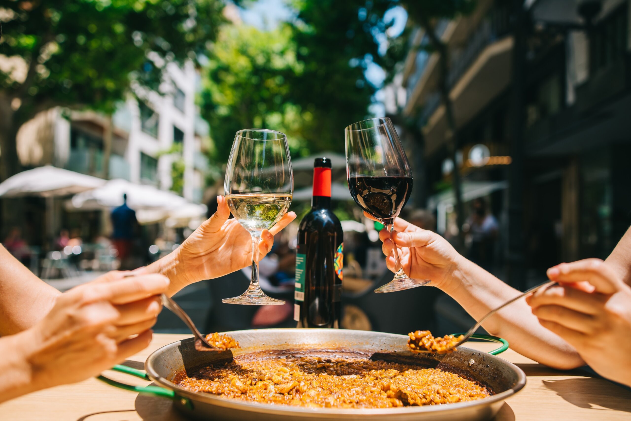 two girls holding drinks wine start eating paella with seafood and squid at a table in a restaurant
