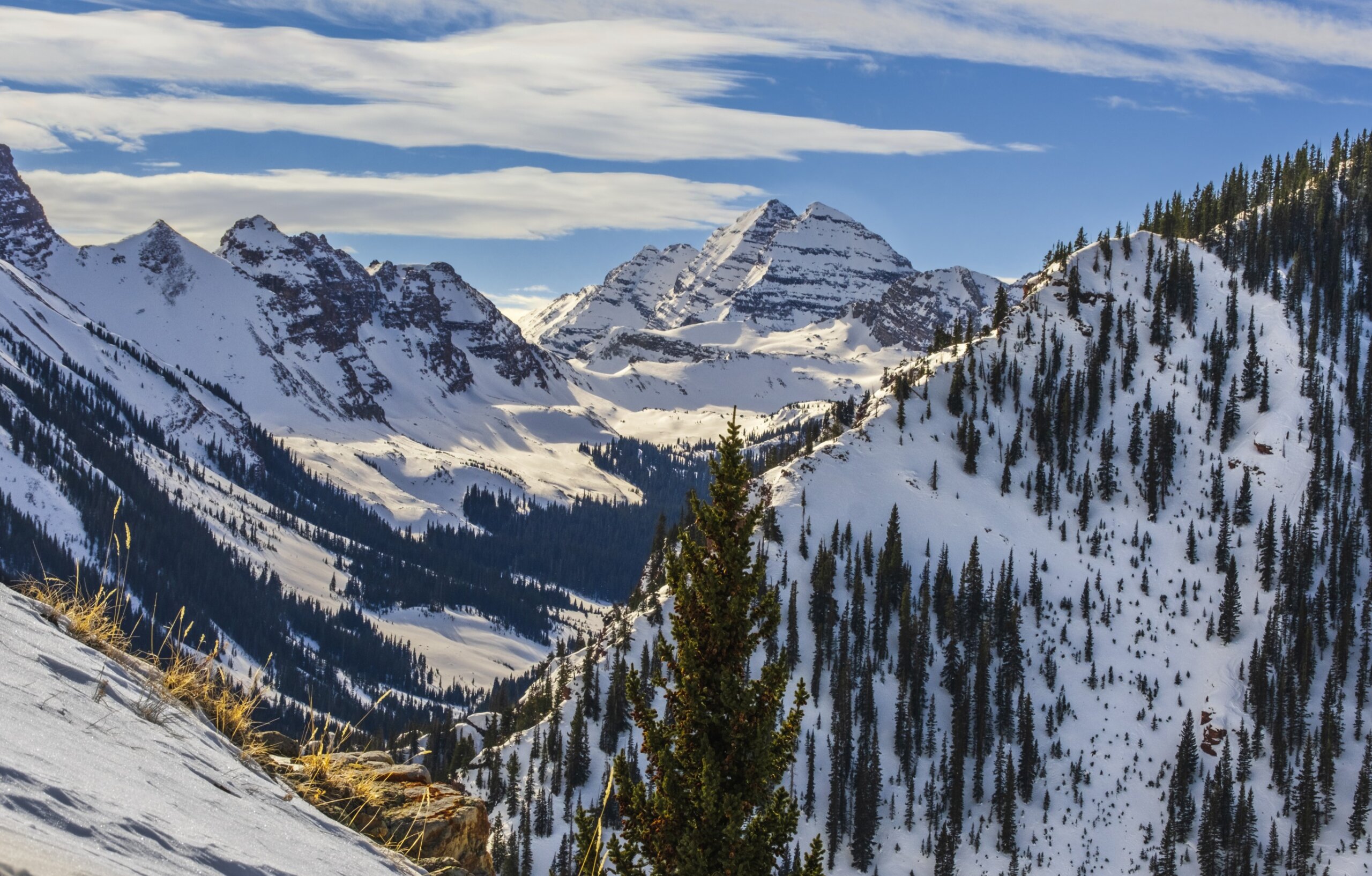 Beautiful view of Aspen, Snowmass mountain range, Colorado, USA, in winter; peaks are covered with snow and pines; blue sky with clouds in background
