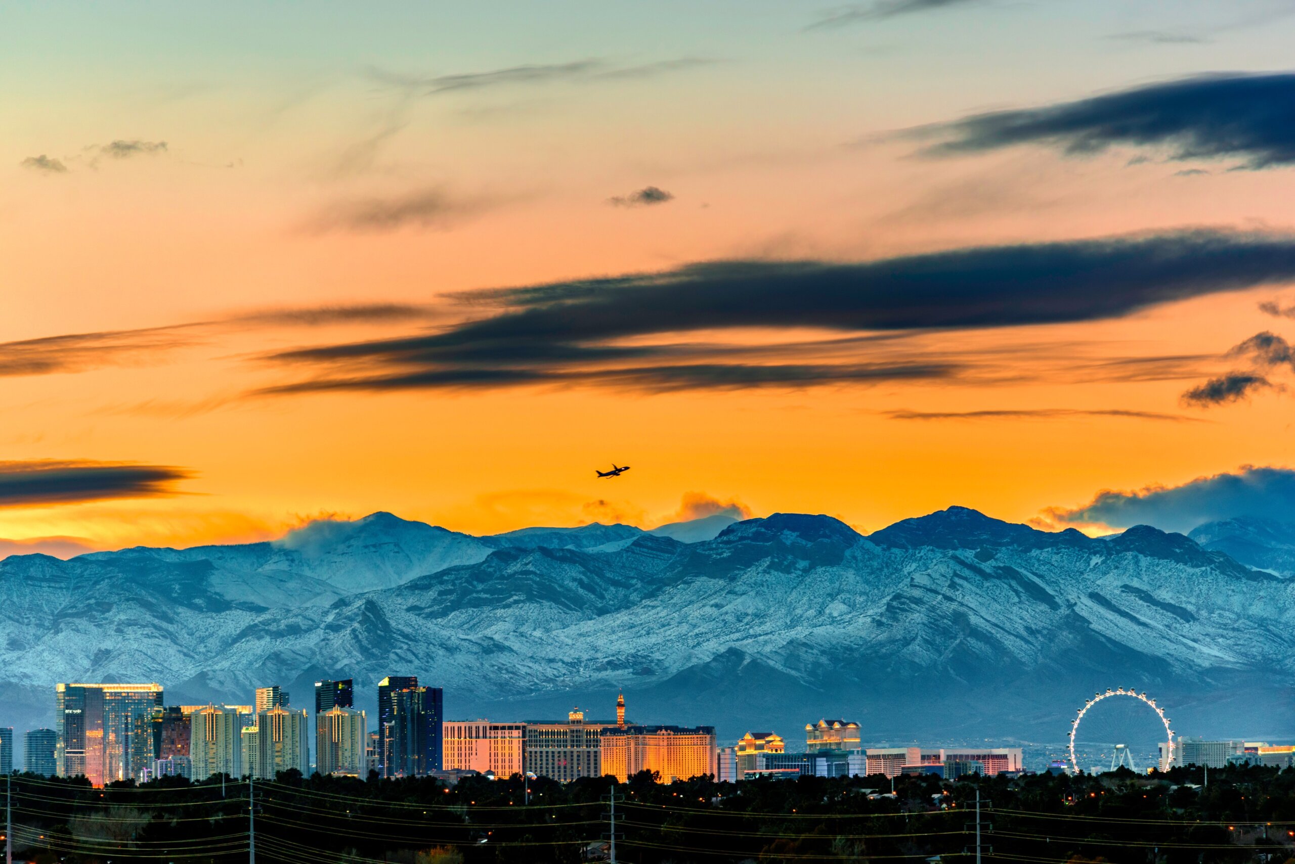 Las Vegas skyline in winter snow capped mountain and a jet plane taking off in the sunset sky
