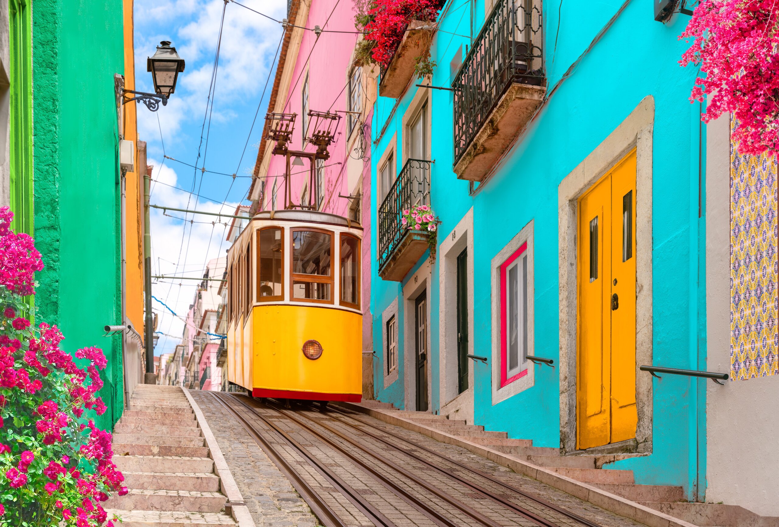 European Overtourism concept: Lisbon, Portugal - Yellow tram on a street with colorful houses and flowers on the balconies - Bica Elevator going down the hill of Chiado.
